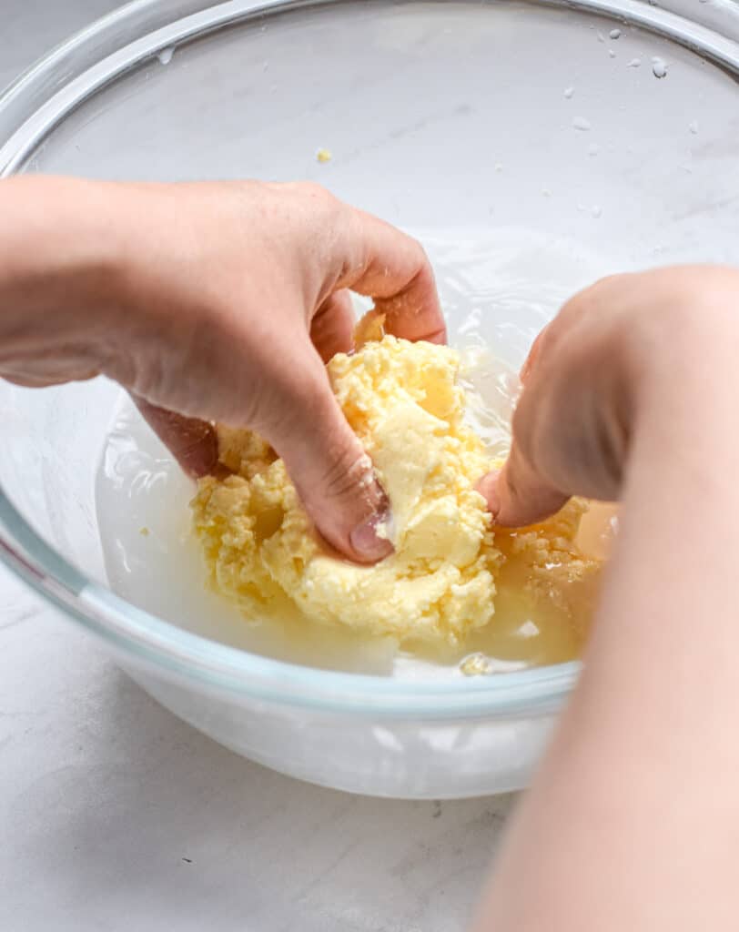 hands squeezing butter in a glass bowl with fingers to extract buttermilk