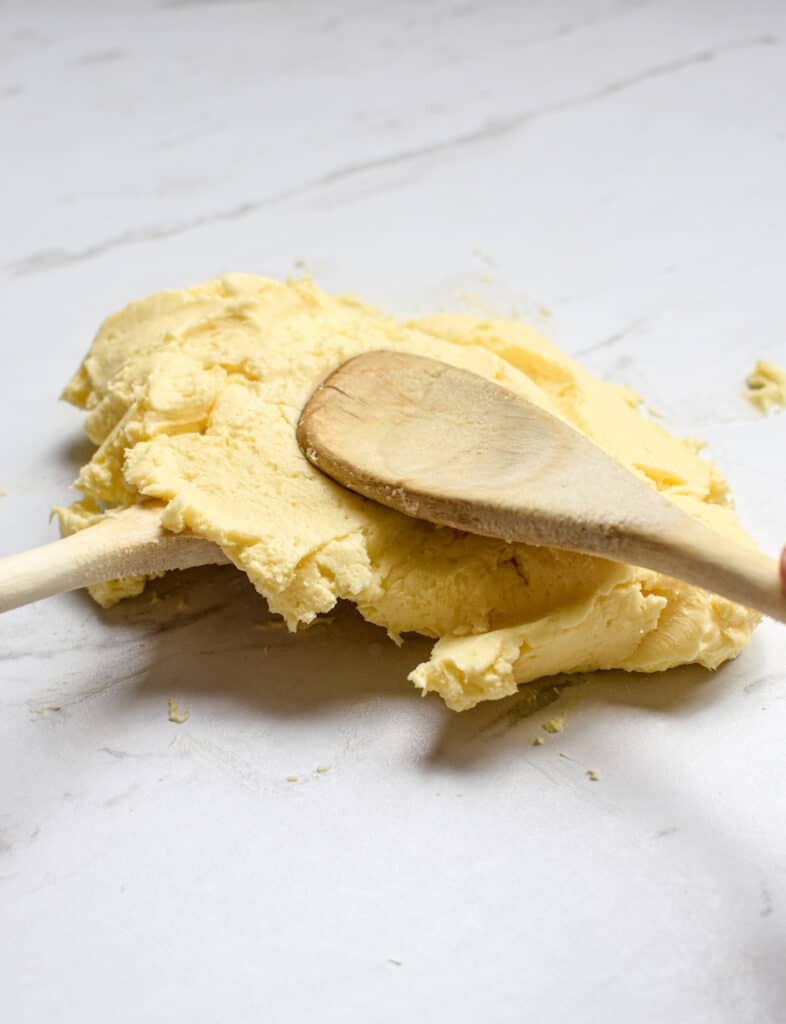 close up of wooden spoons shaping yellow butter on a white bench