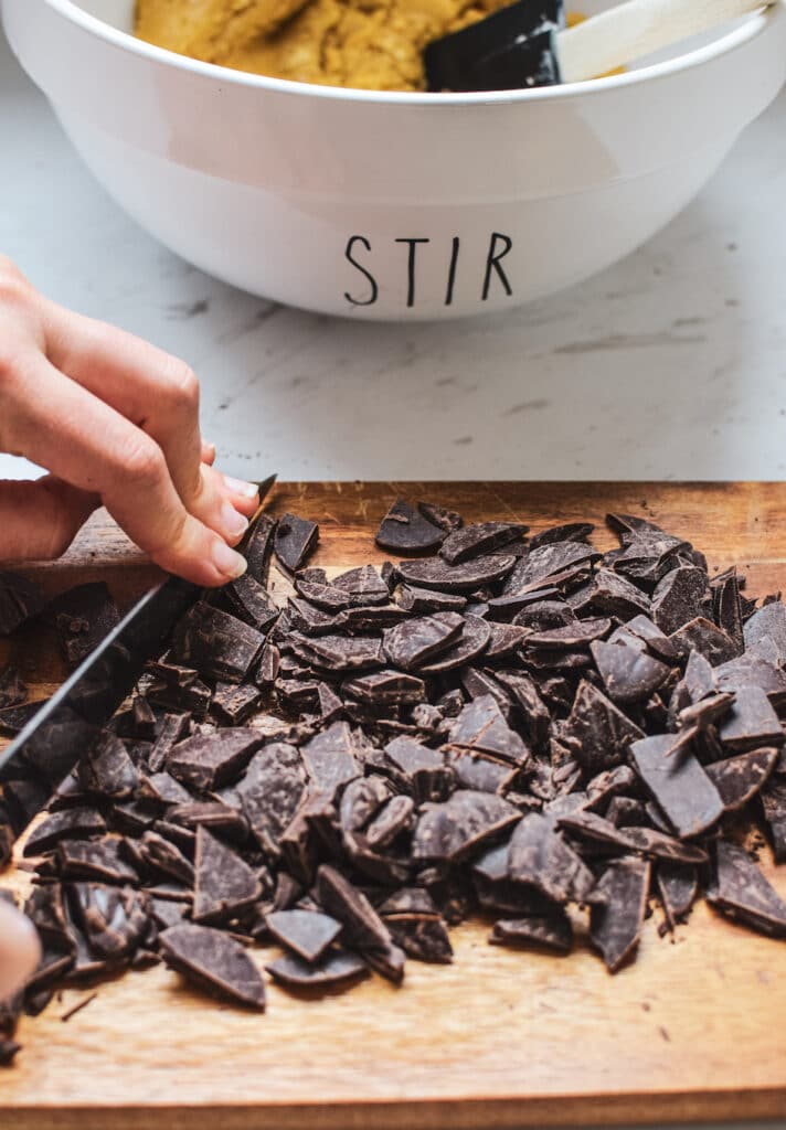 Chocolate chunks being chopped on a wooden board. A bowl with the word 'Stir' on it in the background