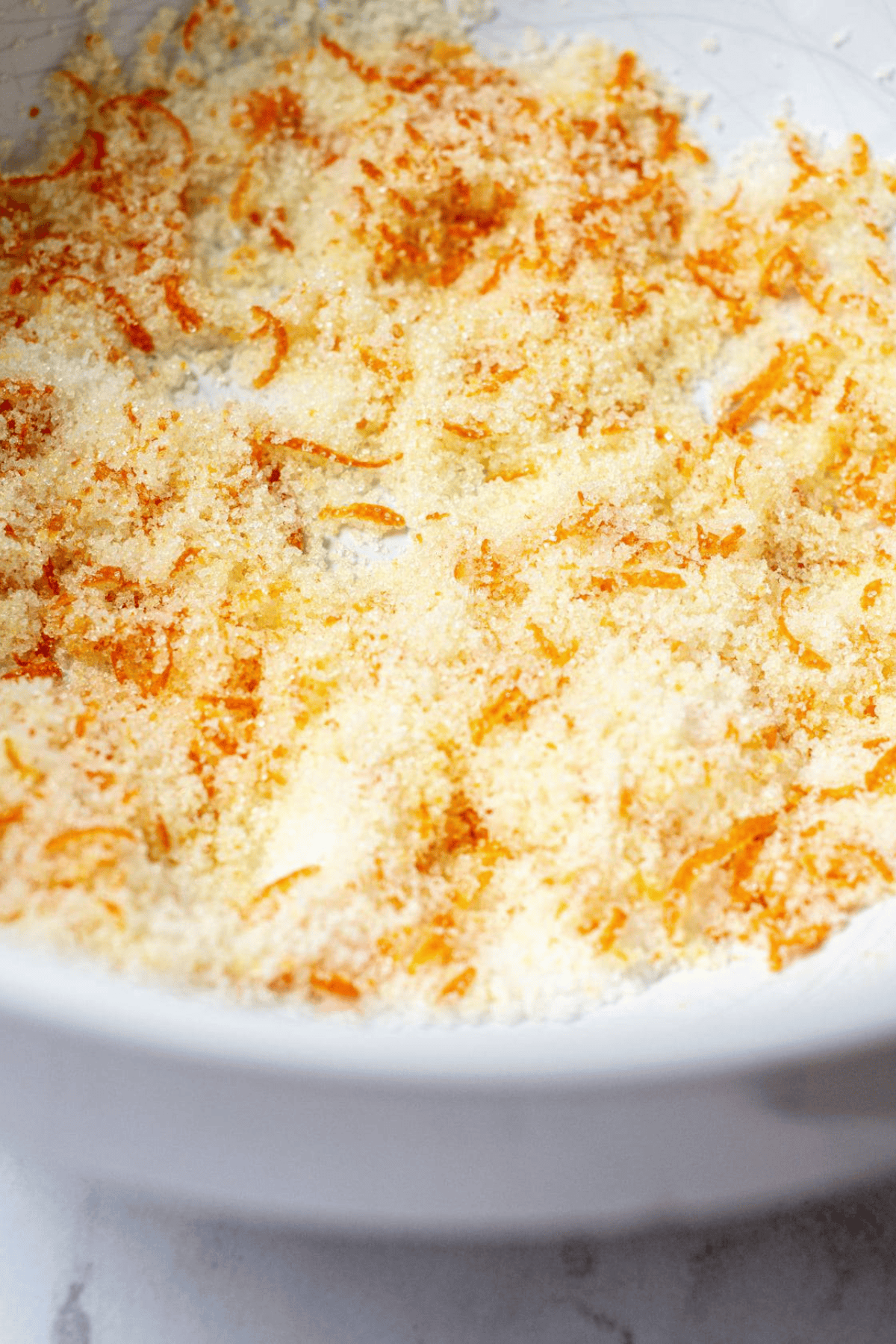 A close-up of a white bowl containing a mixture of orange zest and granulated sugar, with a textured, crumbly appearance—perfect for adding to homemade scones.
