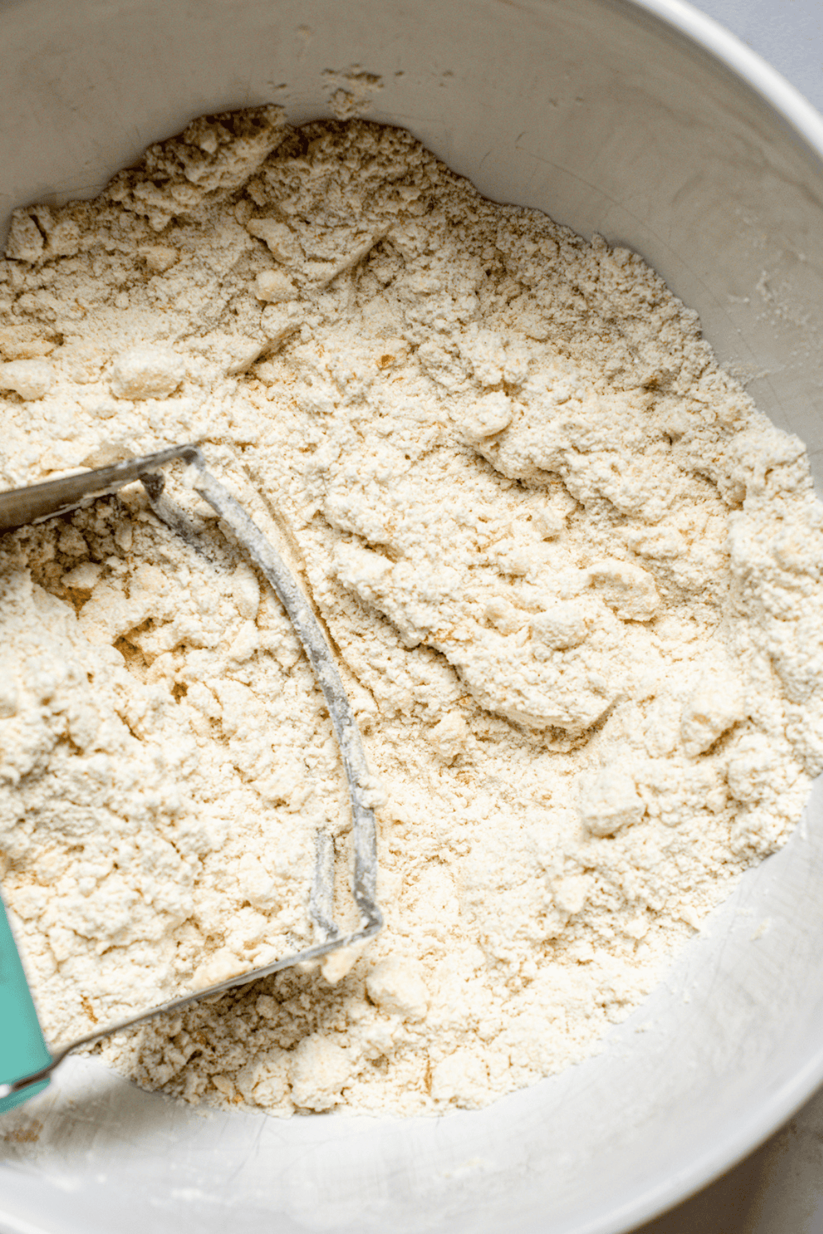 A bowl of dry biscuit dough ingredients being cut together with a pastry cutter, creating a crumbly texture perfect for homemade scones.