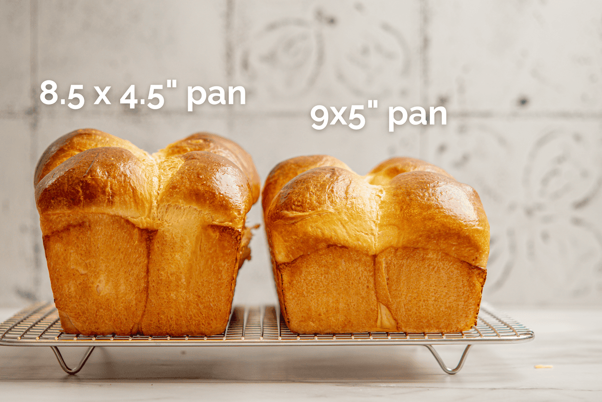 Two loaves of bread, made from a classic brioche bread recipe, sit side by side on a cooling rack. The left loaf is in an 8.5 x 4.5 inch pan, while the larger right loaf uses a 9 x 5 inch pan. Labels show the distinct pan sizes.