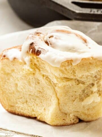 a close up of a baked brioche cinnamon roll with a fork in the foreground and a cast iron pan in the background