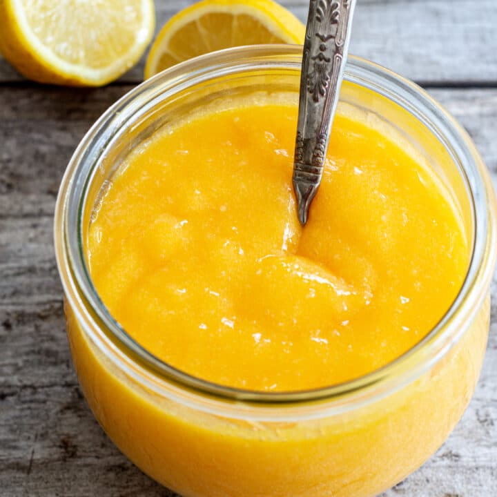 a close up look at a Weck jar of lemon curd with a silver spoon in the middle. On a wooden board