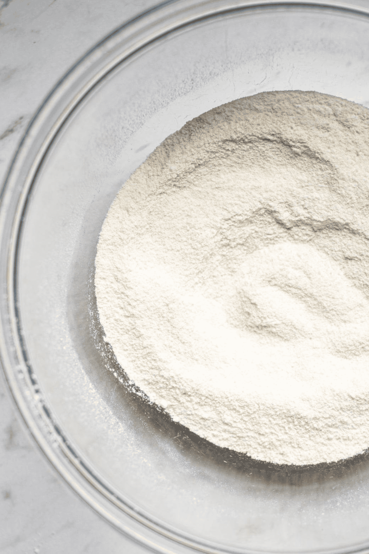 A clear glass bowl filled with a mound of white flour sits on a light-colored surface, ready for your easy macaron recipe.