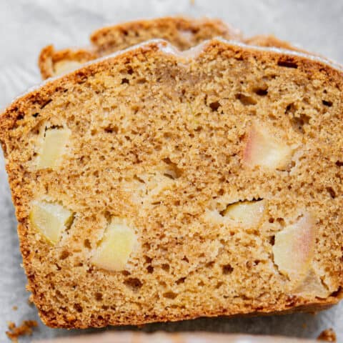 A close-up of a sliced loaf of apple bread, showing a moist, golden-brown crumb with visible chunks of apple throughout.