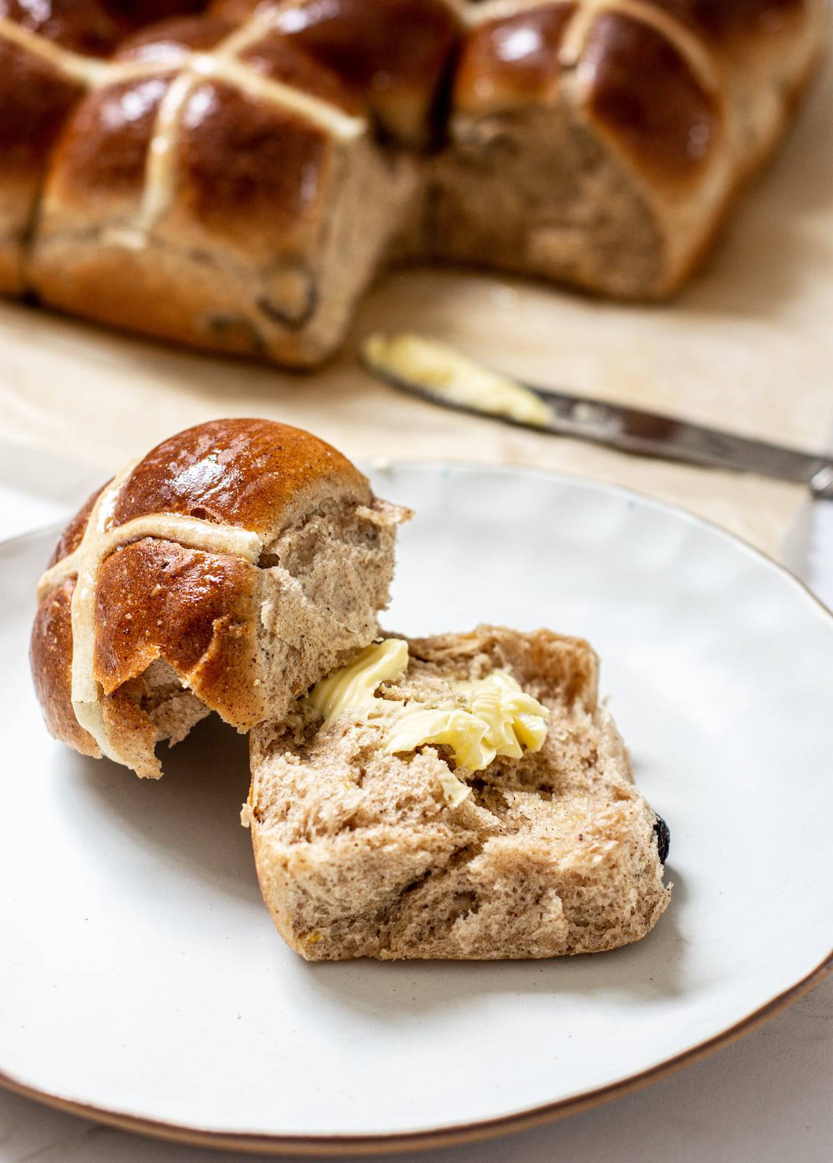 a plate with a buttered hot cross bun, other buns are in the background