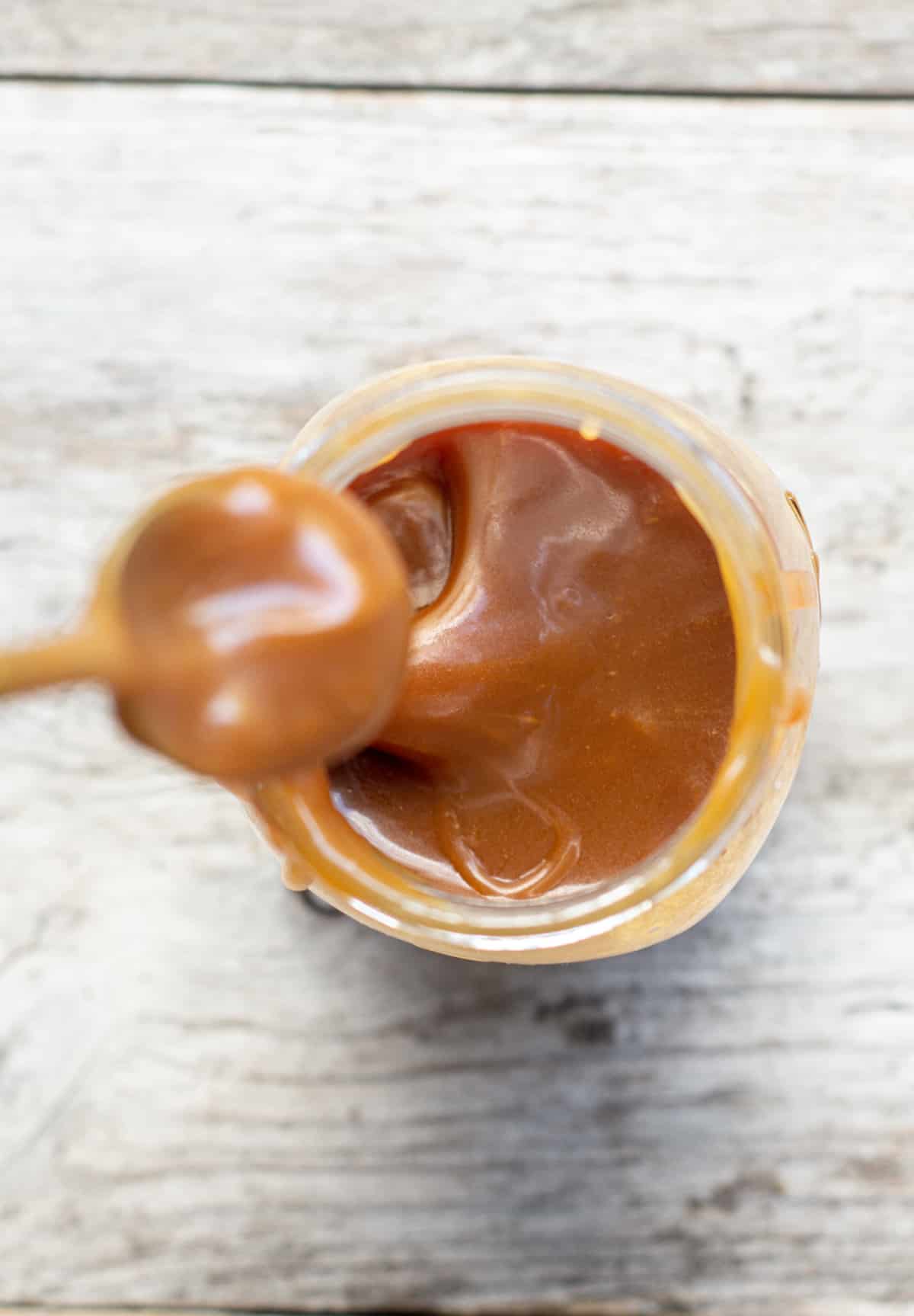 a birds eye view of a jar of caramel sauce with a caramel covered spoon dipped in