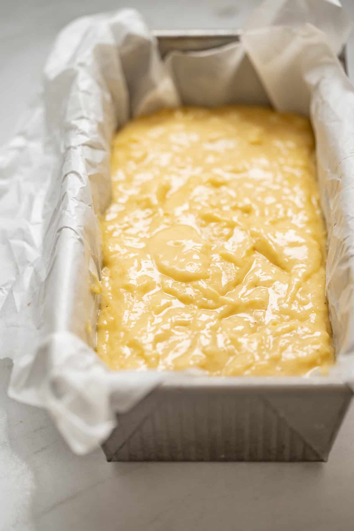 A metal loaf pan lined with parchment paper is filled with unbaked yellow batter for a lemon yogurt olive oil cake, ready to go into the oven.