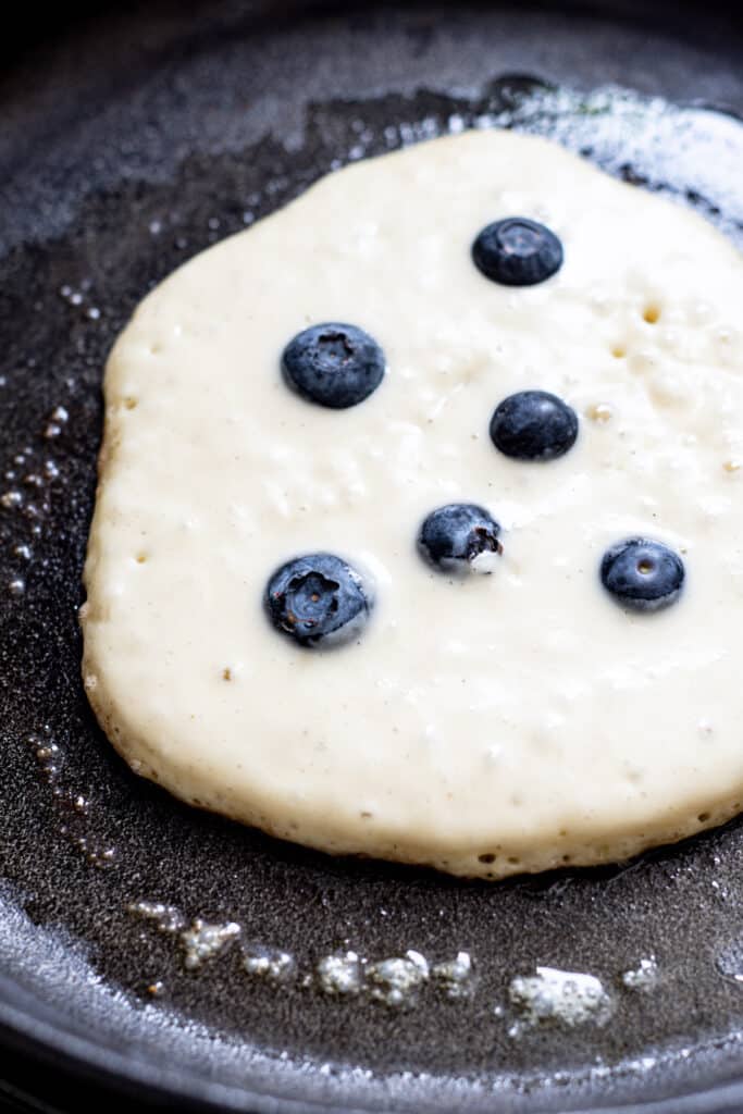 a half cooked pancake with fresh blueberries