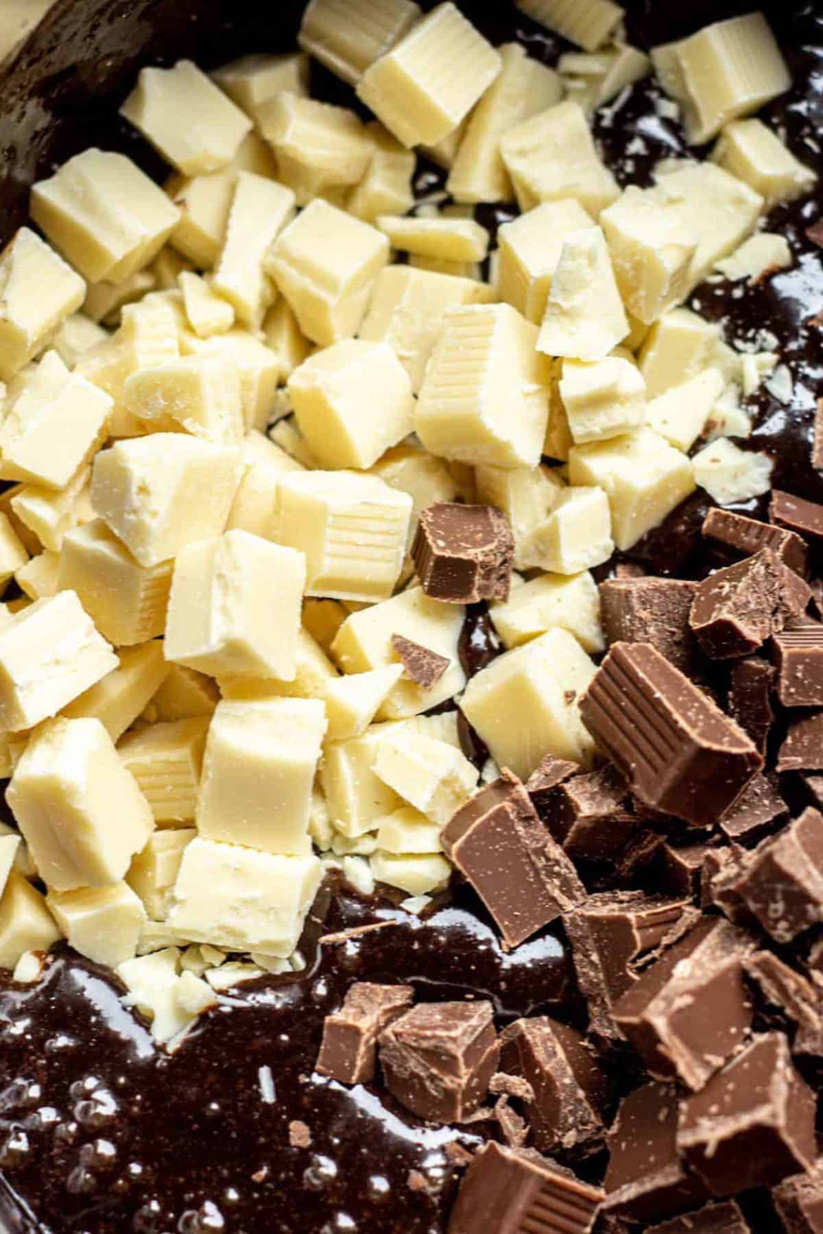 Close-up of chopped white and milk chocolate pieces on top of a dark brownie batter, ready to be mixed together for decadent triple chocolate brownies.