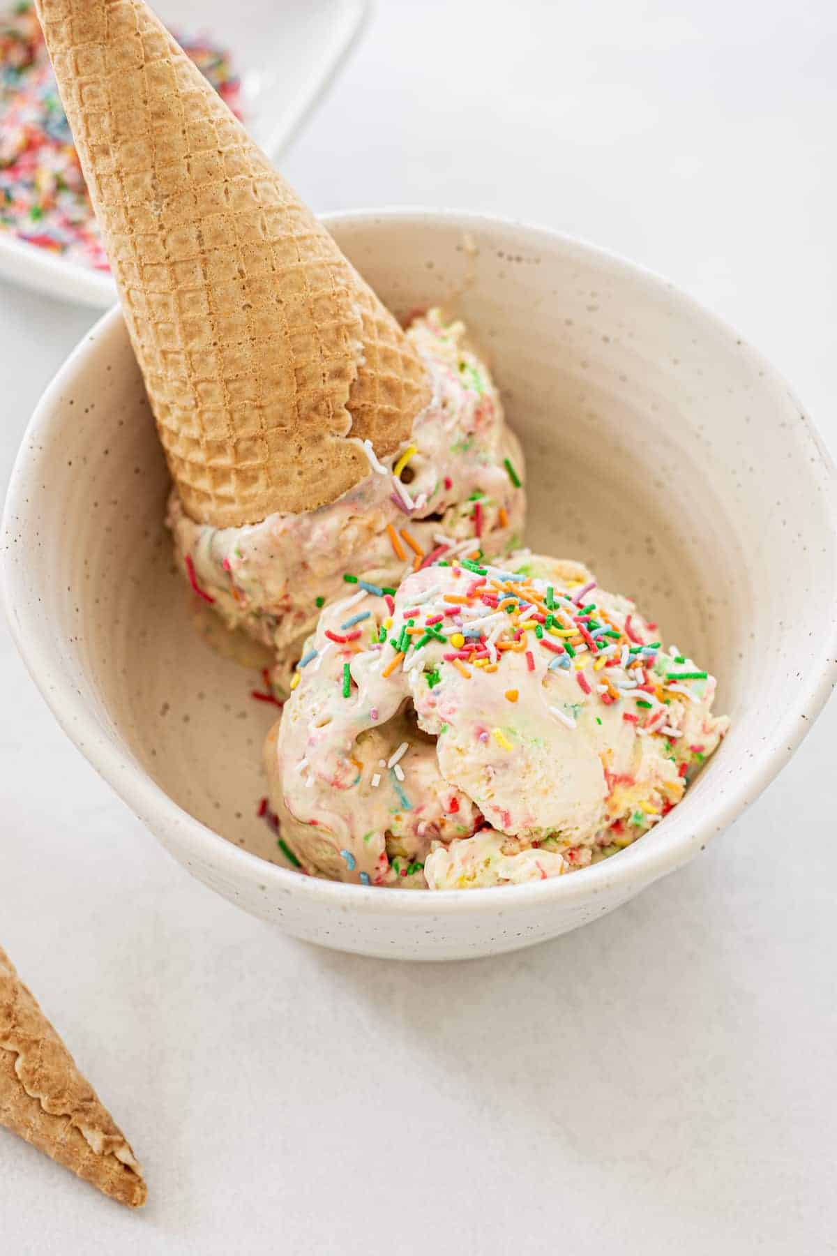 Birthday Cake Ice Cream in a bowl with a waffle cone and funfetti. 