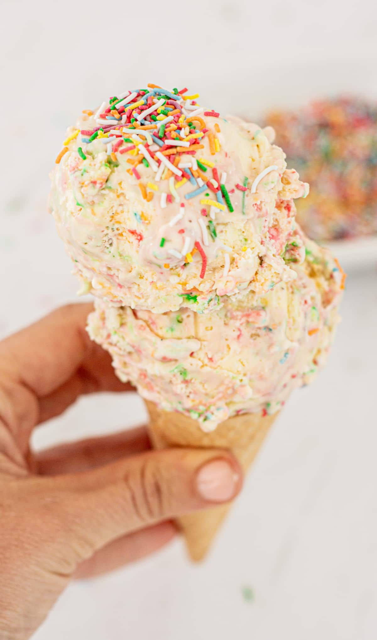 a hand holding a double scoop of sprinkle ice cream.