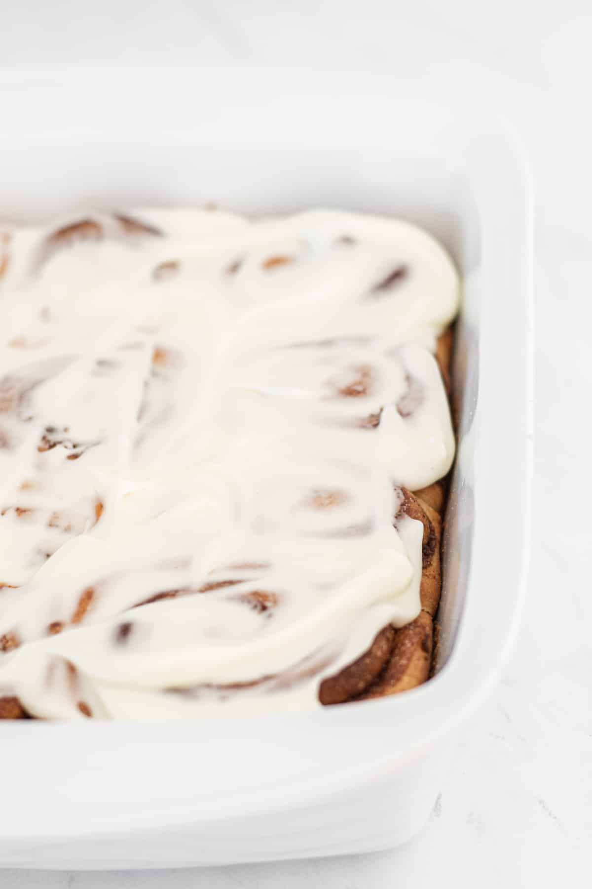 Cinnamon rolls with condensed milk and topped with cream cheese icing in a baking tray.