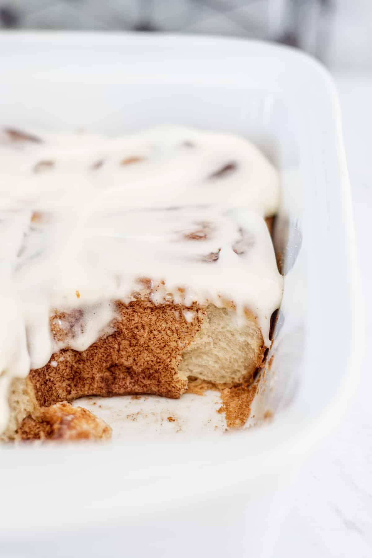 cinnamon rolls in a white tray with one removed, dripping with icing .