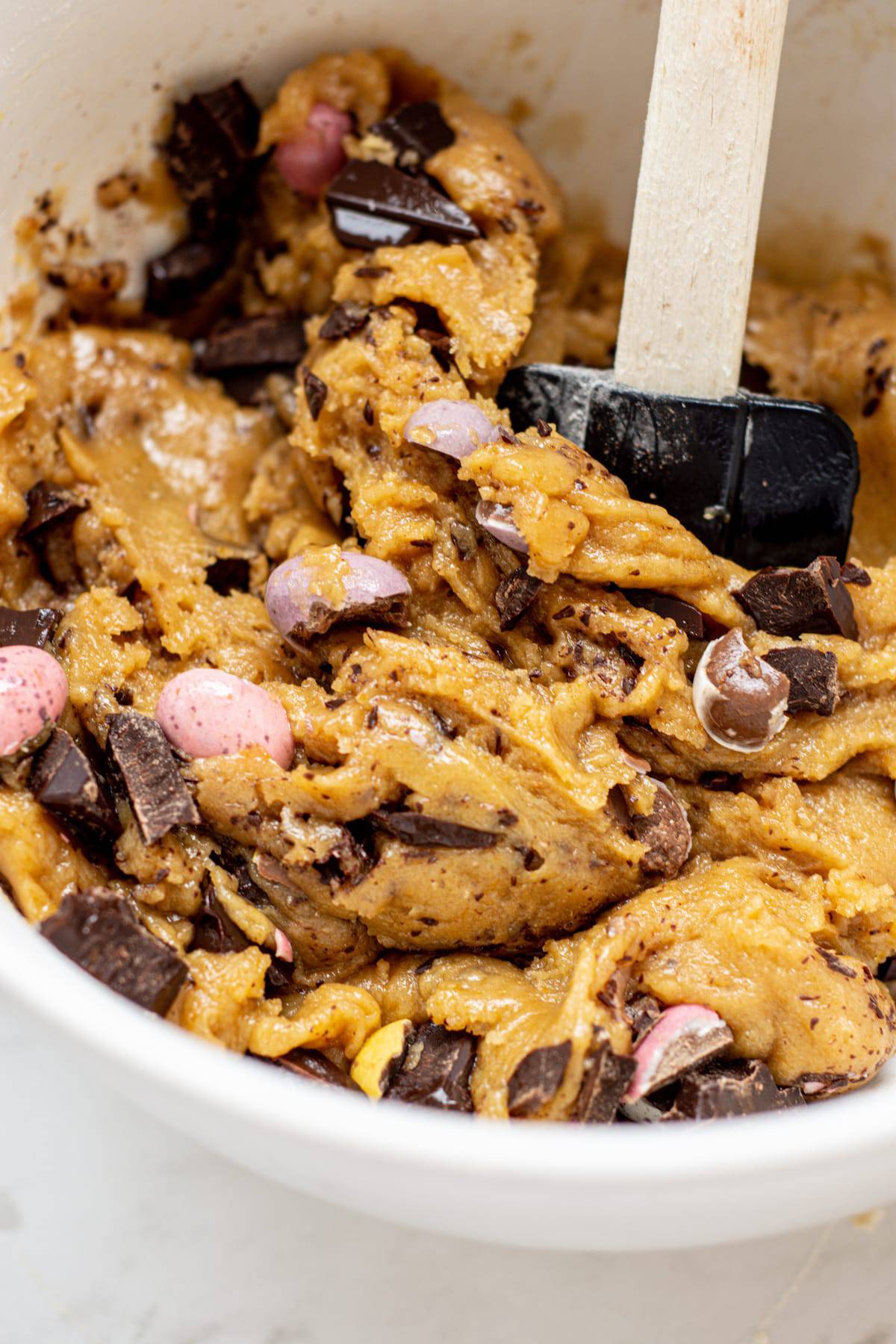 a bowl of cookie dough with chopped chocolate and mini eggs.