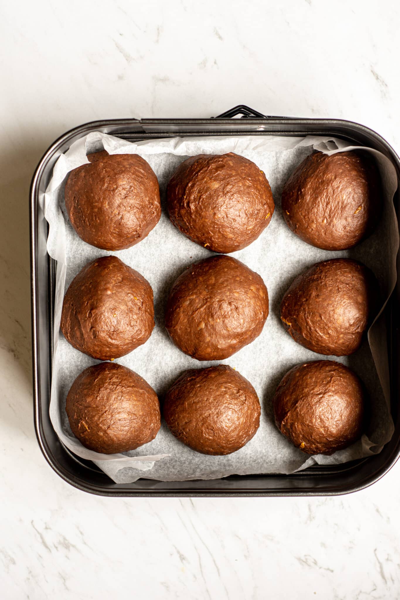 9 unbaked and unrisen orange hot cross buns in balls in a tray.