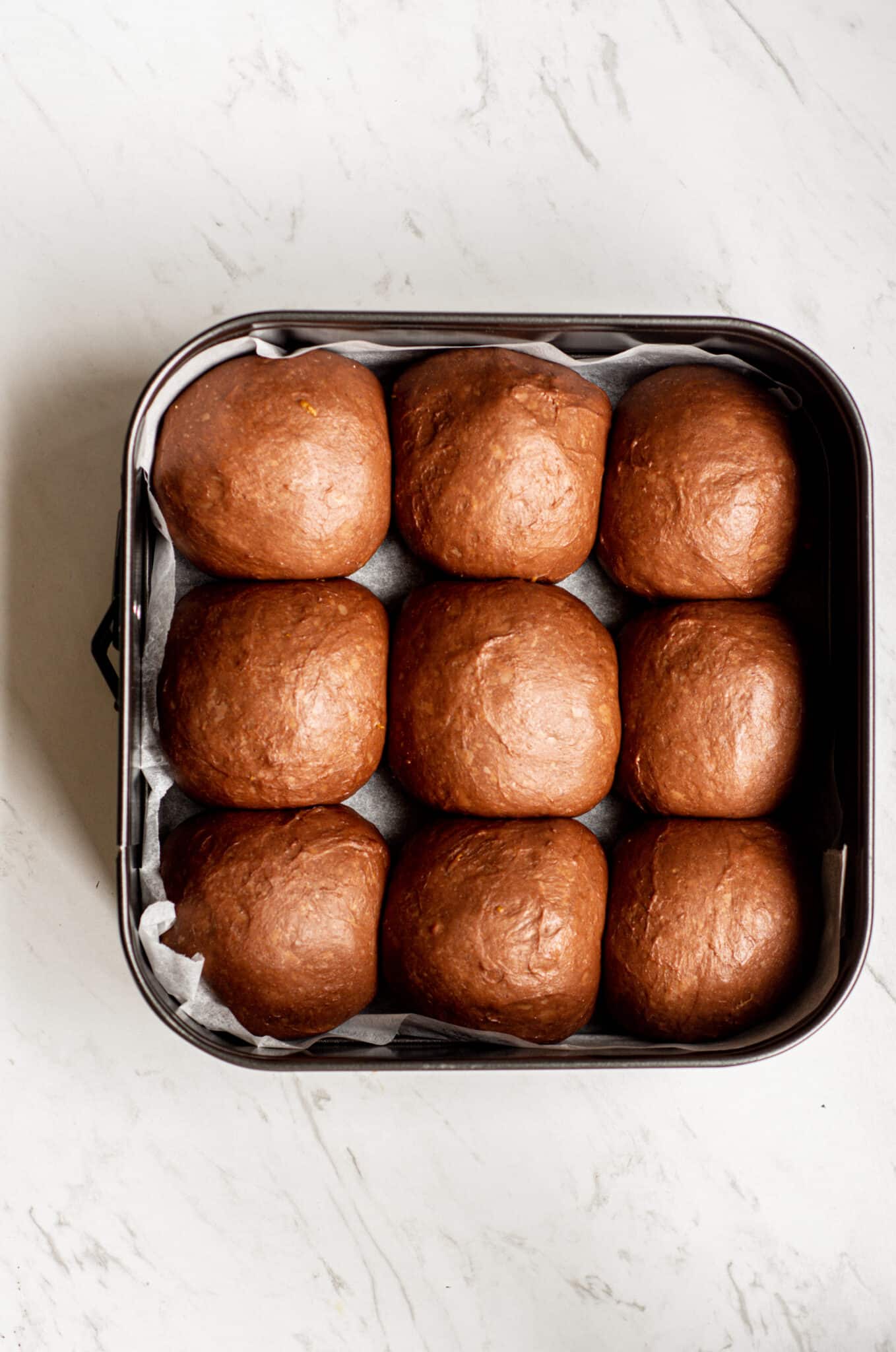 9 unbaked orange hot cross buns in balls in a tray.