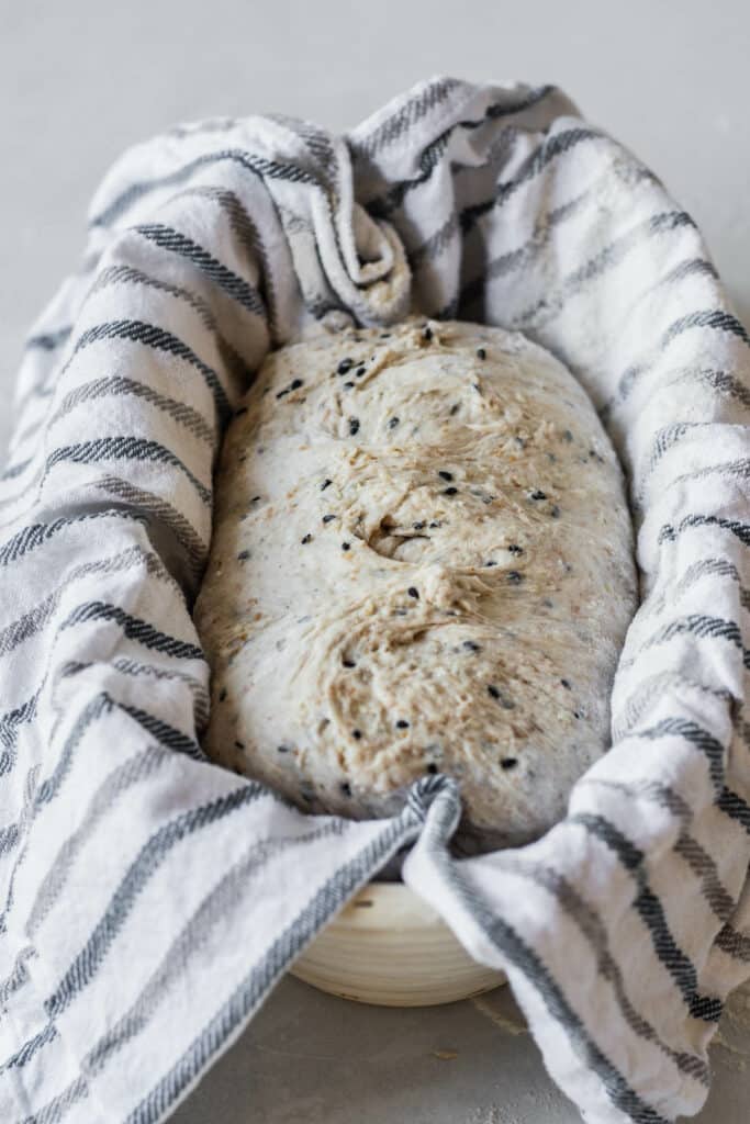 a shaped sesame sourdough loaf in a towel lined basket.