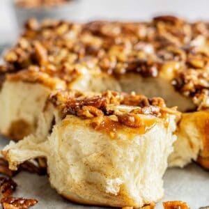 A close-up of a gooey small batch sticky bun topped with chopped pecans and caramel glaze, with a soft, fluffy interior visible where a piece has been pulled apart.