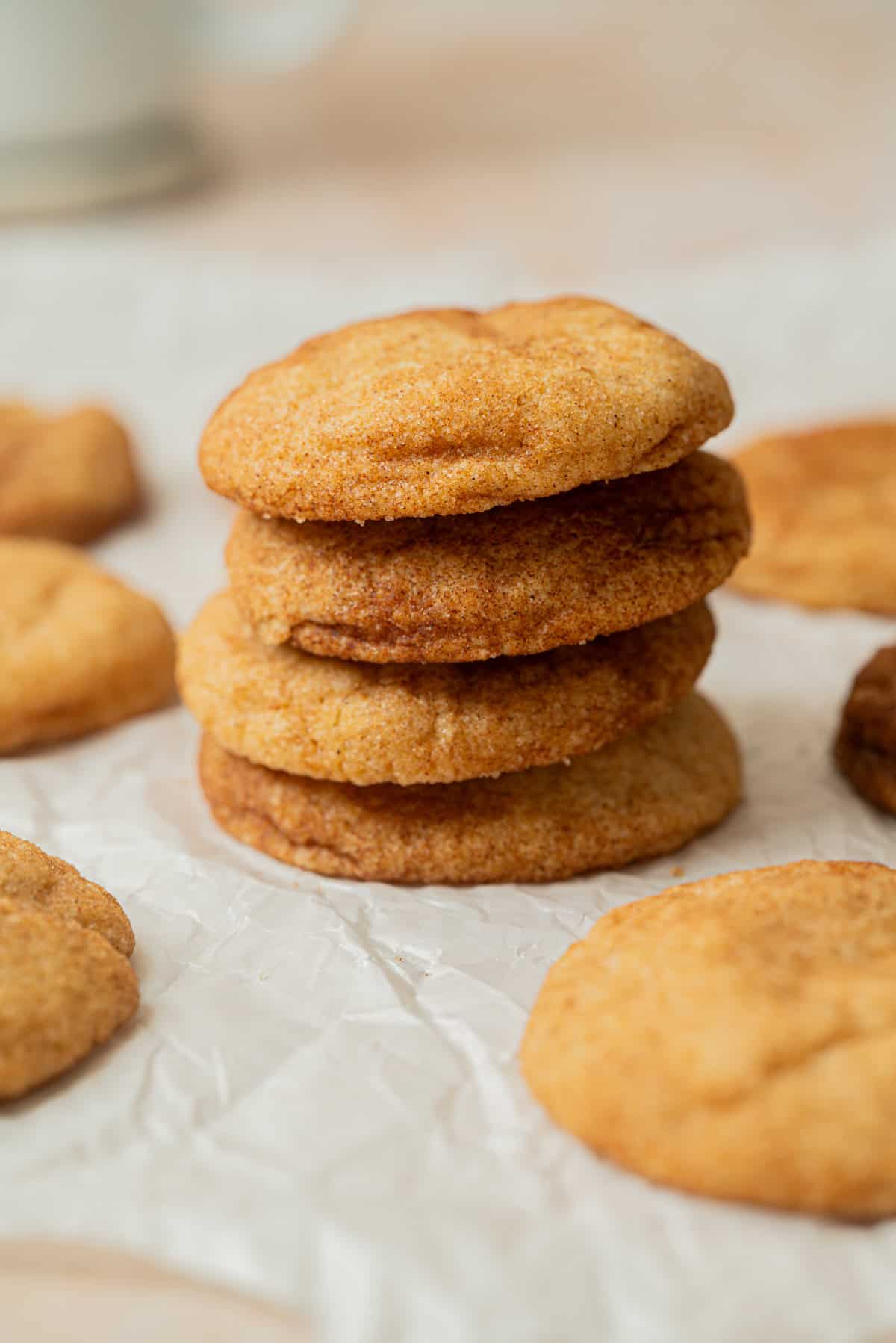 A stack of golden-brown Small-Batch Snickerdoodles sits on crinkled parchment paper, surrounded by more cookies. The cookies have a soft, slightly cracked surface with a cinnamon-sugar coating.