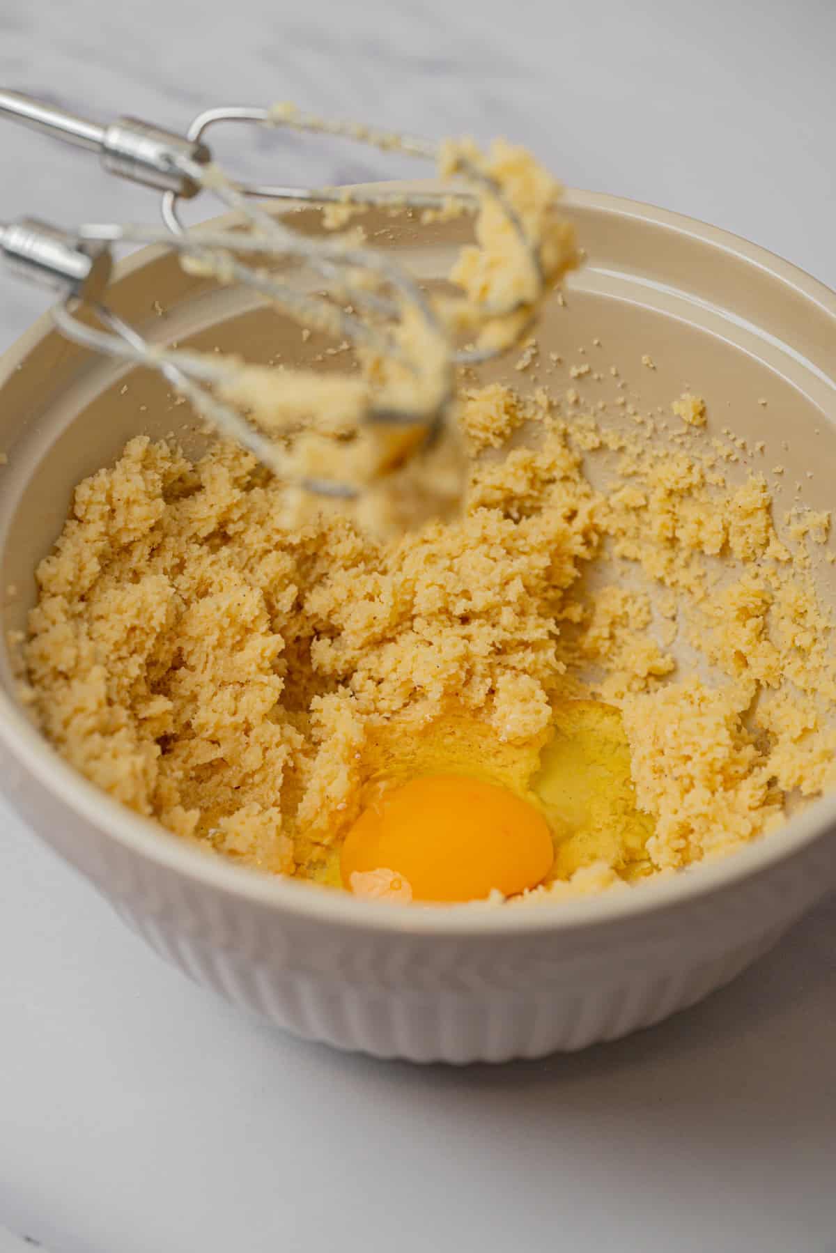 A mixing bowl with creamed butter and sugar, an egg cracked on top, and a hand mixer with some mixture clinging to the beaters rests on the edge—ready to whip up irresistible Small-Batch Snickerdoodles.