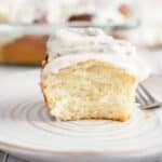 Sourdough cinnamon rolls recipe with cream cheese icing in the background while one is on a plate with fork.