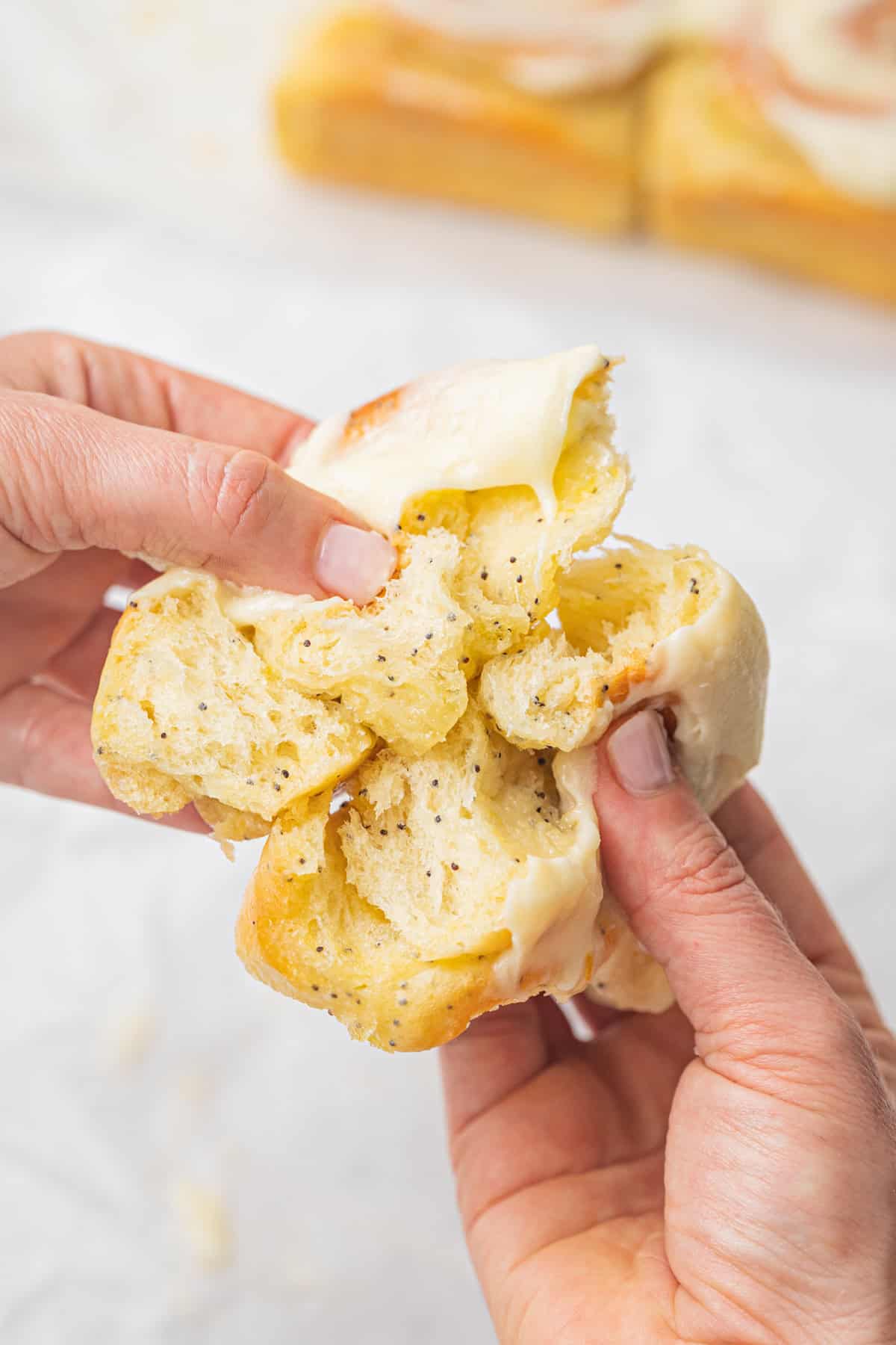 Two hands pull apart a soft lemon poppy seed roll.
