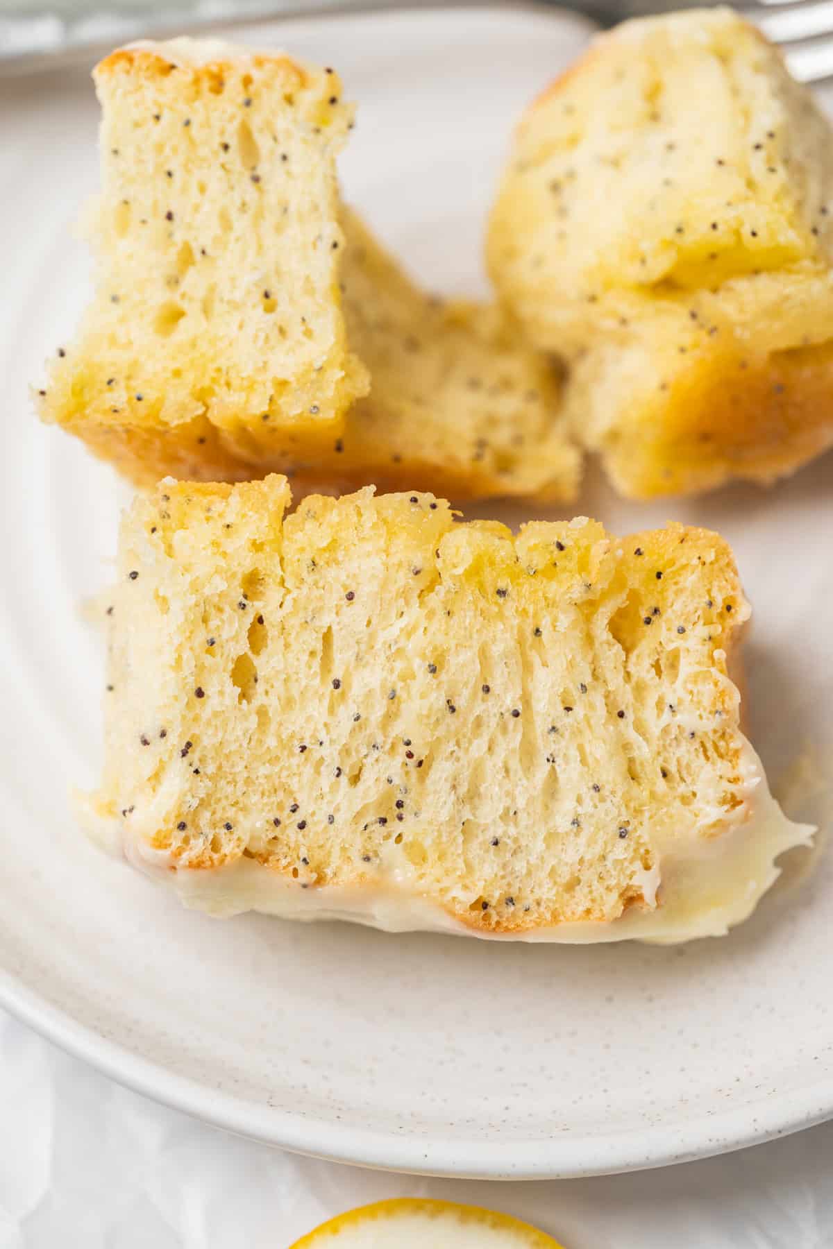 Close-up of three pieces of lemon poppy seed bread with a light glaze, placed on a white plate. The moist, dense slices resemble lemon poppy seed rolls, with visible poppy seeds throughout for added texture and flavor.