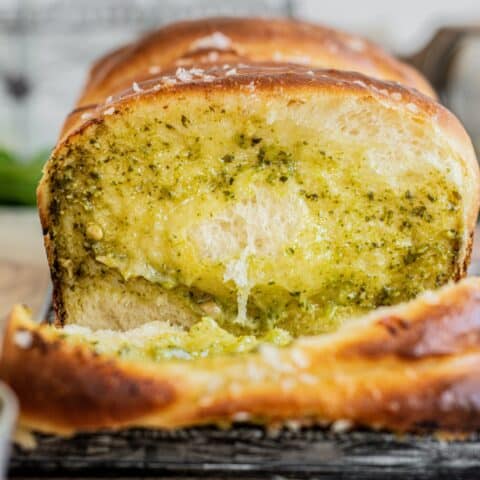 A close-up of pesto bread, a sliced loaf with a golden crust, filled with melted cheese and green pesto, showing a soft and fluffy texture.