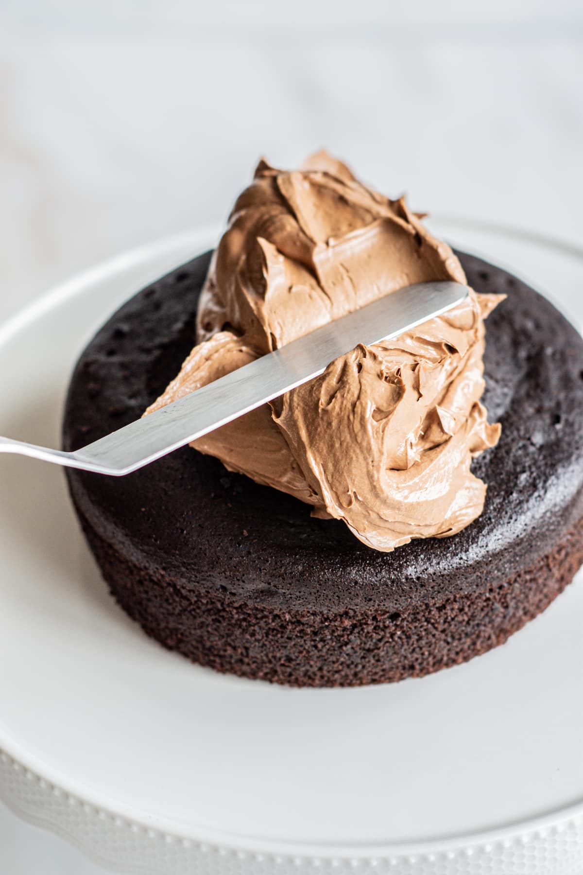 A spatula spreading swiss meringue on a chocolate cake.