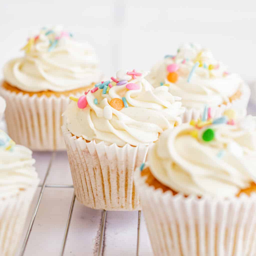 5 cupcakes with white icing and sprinkles.