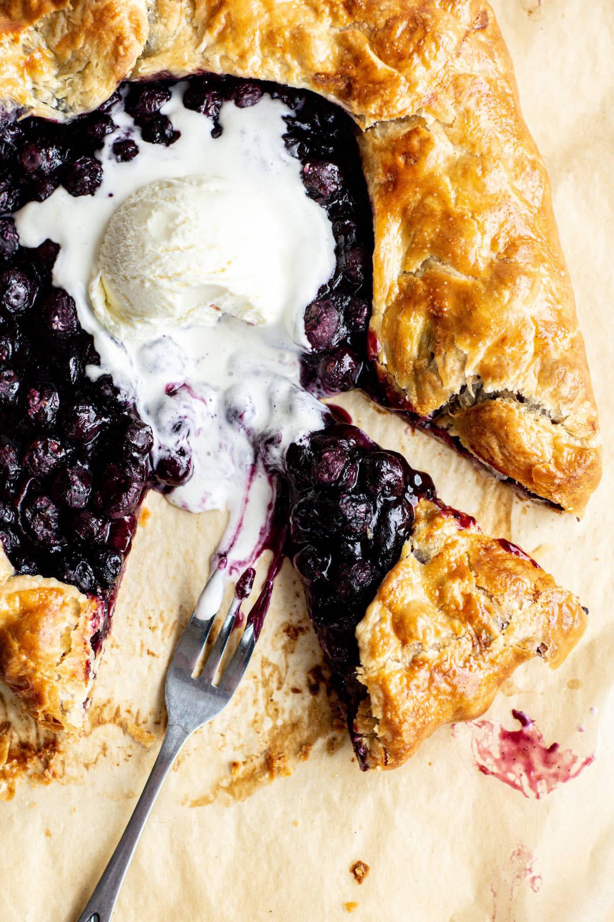 a slice of blueberry galette with a fork and melted ice cream
