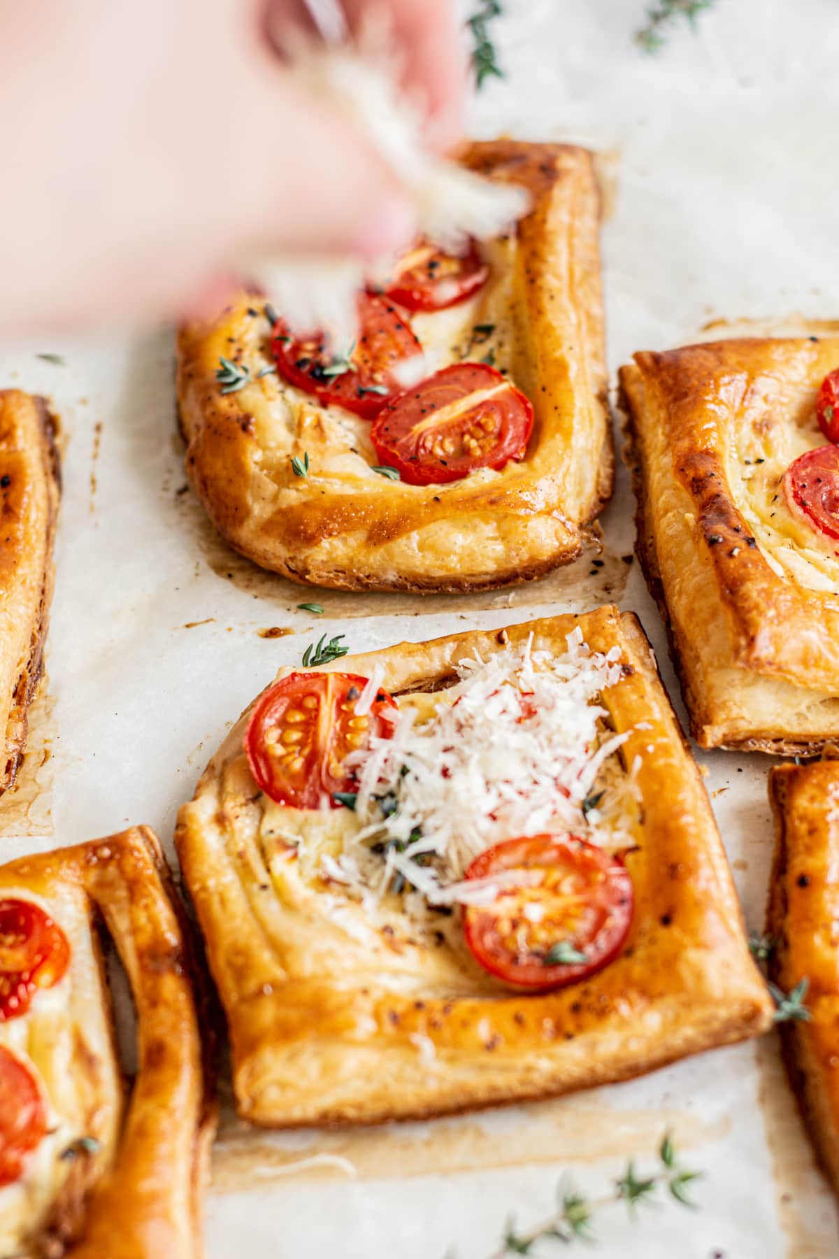 a hand sprinkling parmesan cheese on puff pastry tomato tartlets.