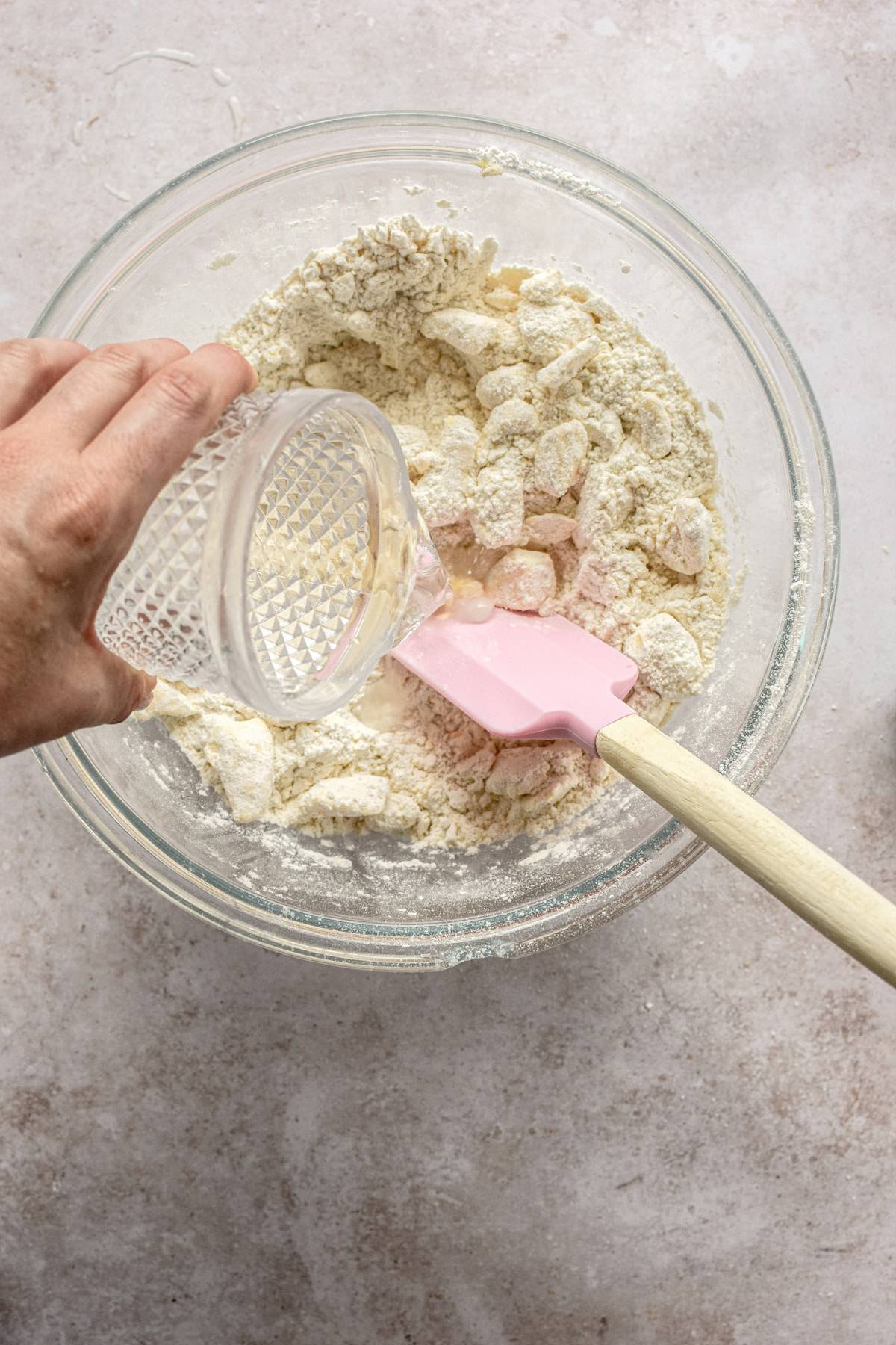 a hand pouring water into a bowl of dough.