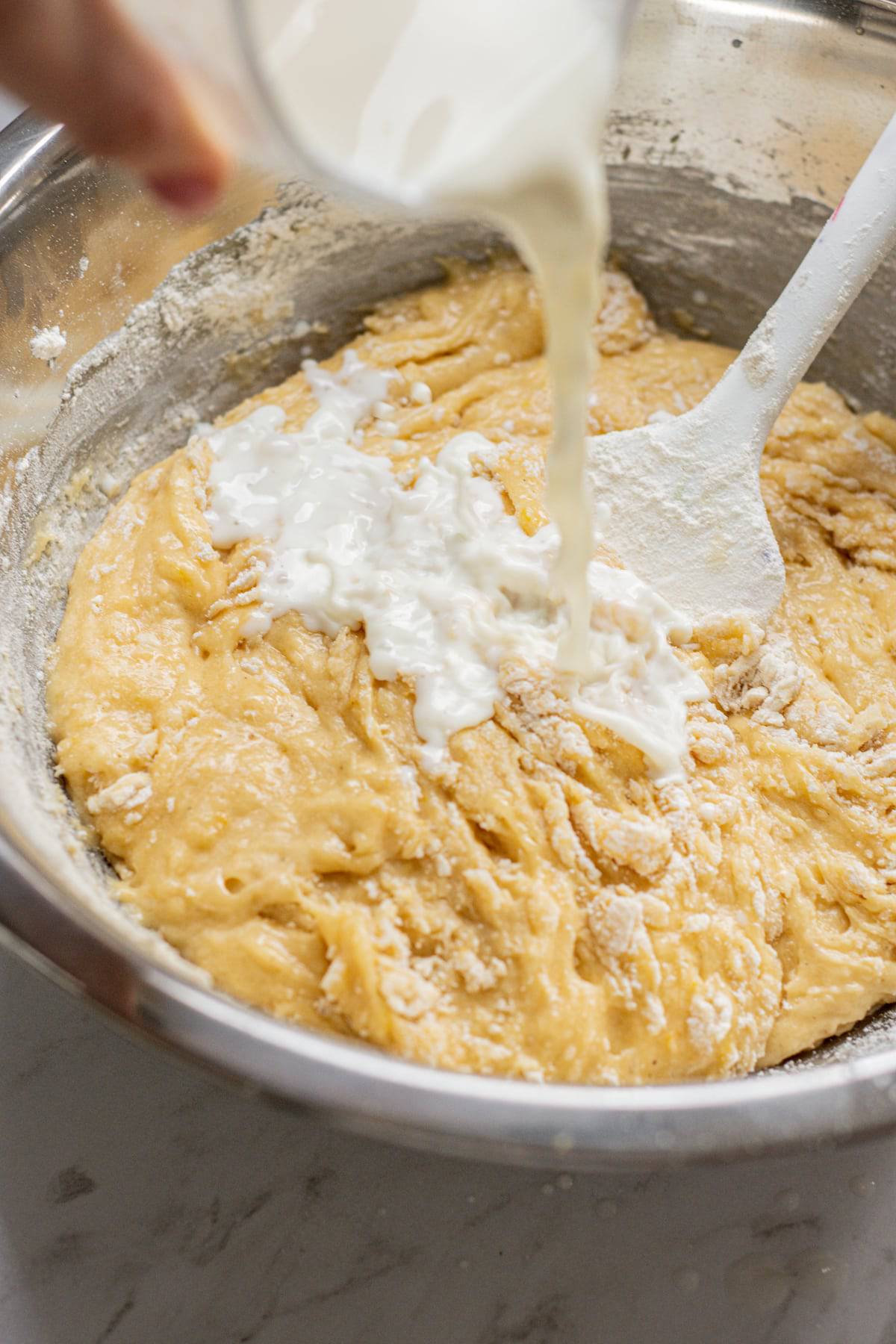 a hand pouring milk into a bowl of dough.