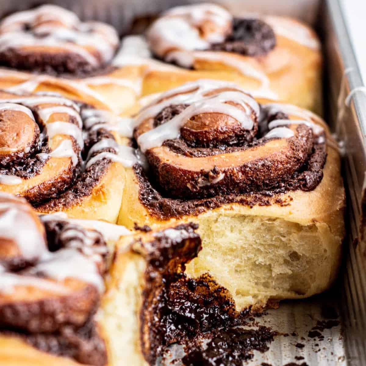 Close-up of chocolate cinnamon rolls in a baking tray with one missing.