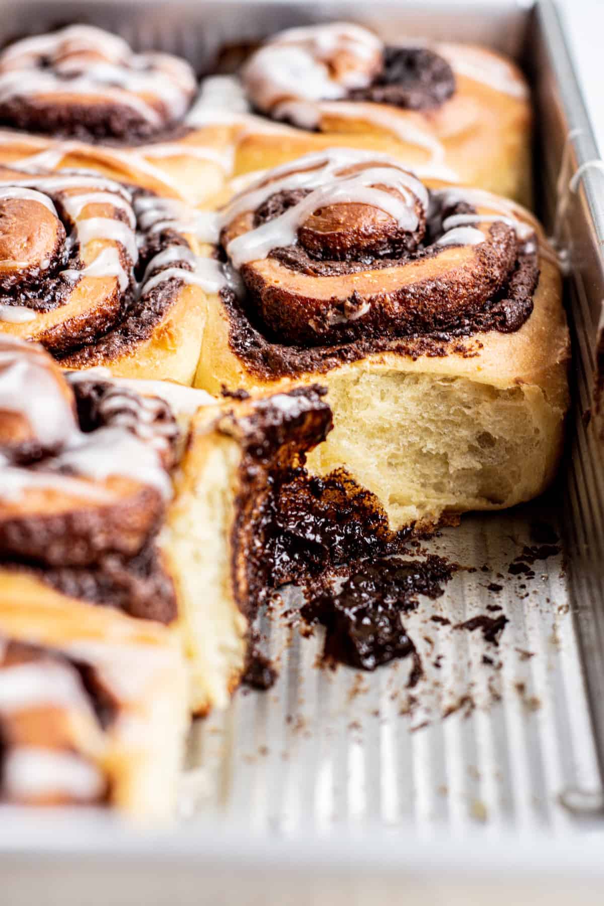 Close-up of fluffy chocolate cinnamon rolls in a baking tray with one missing.