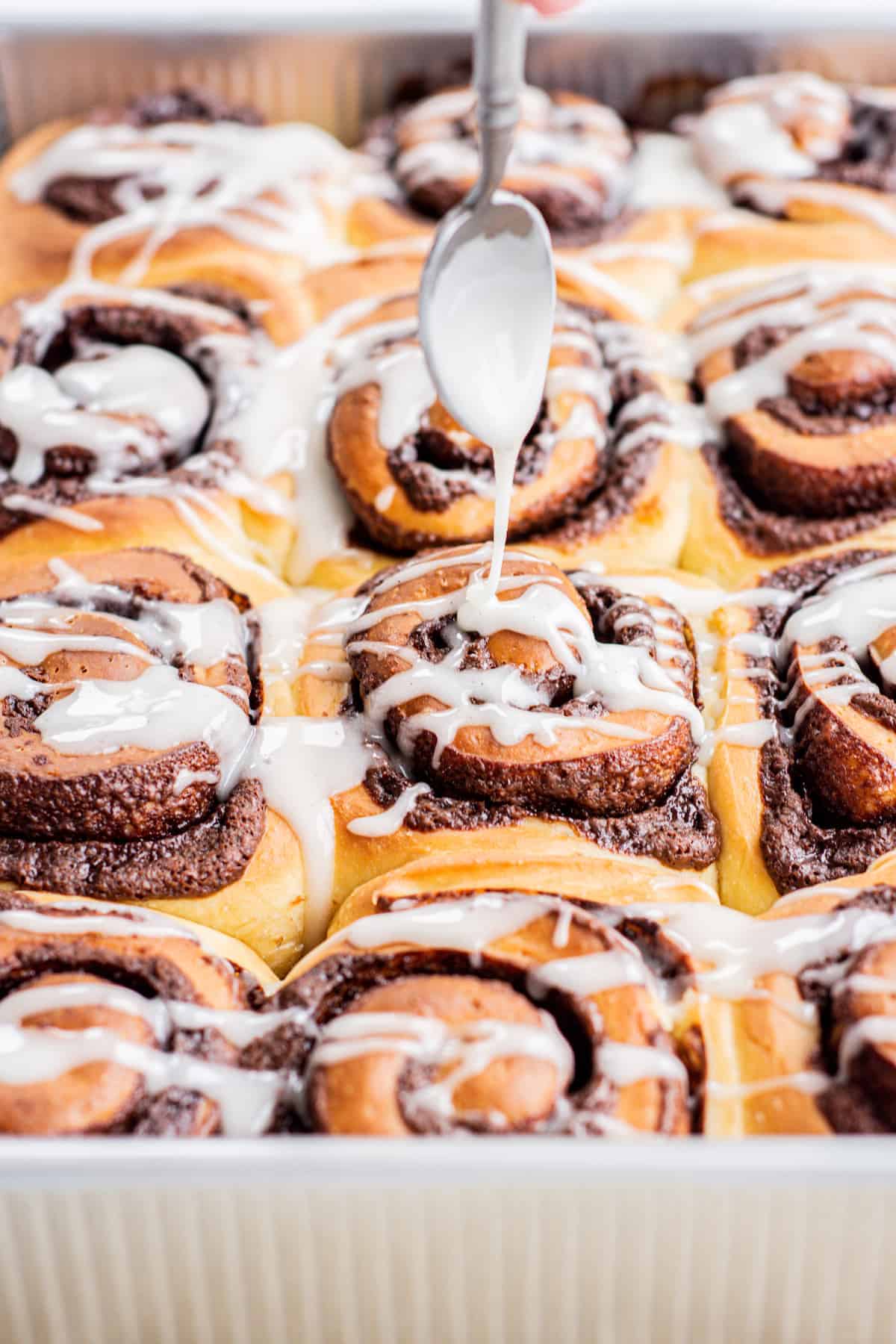 A tray of easy chocolate cinnamon rolls with a glaze being poured over them.