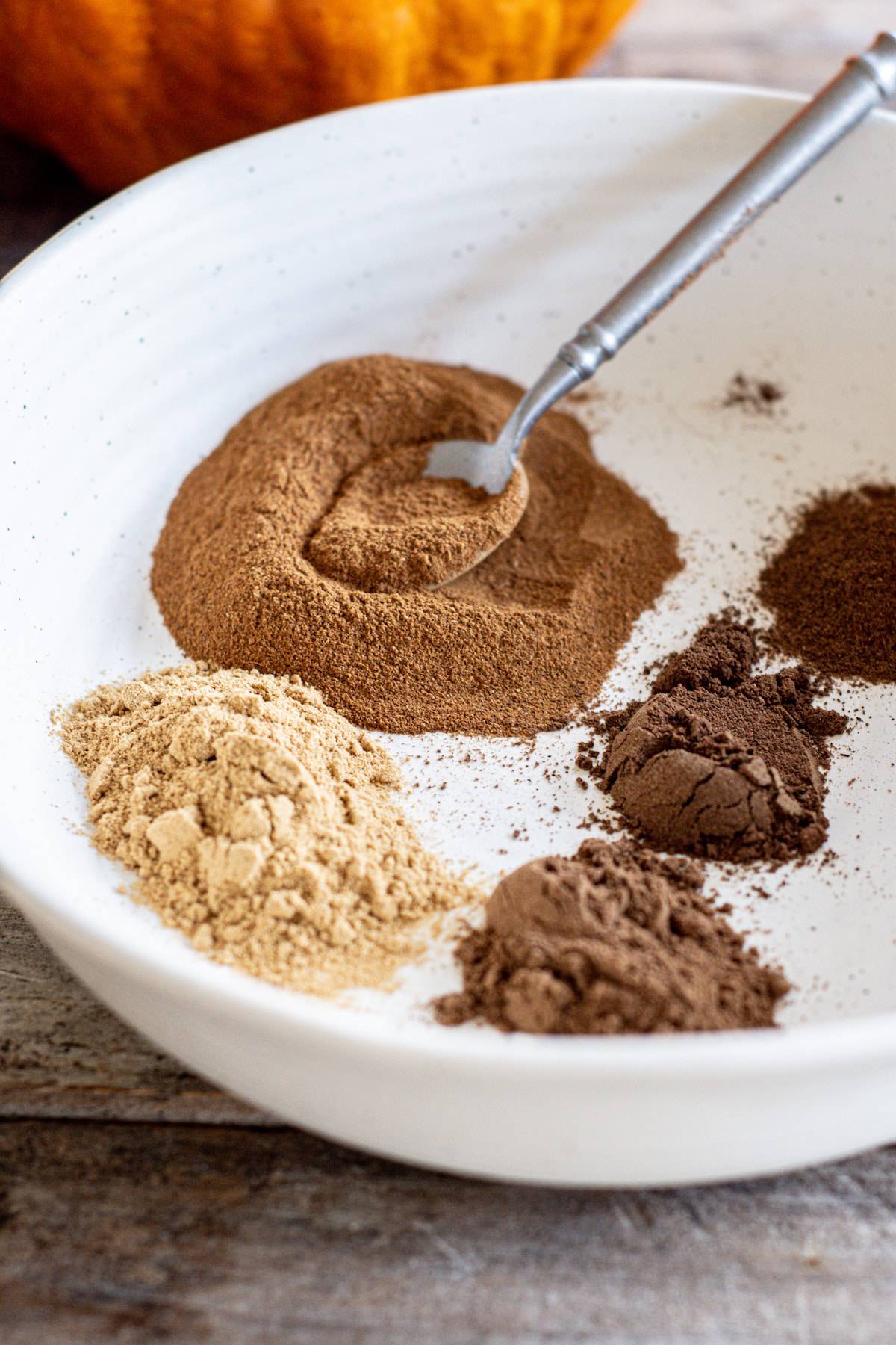 5 types of ground spices in a white bowl.