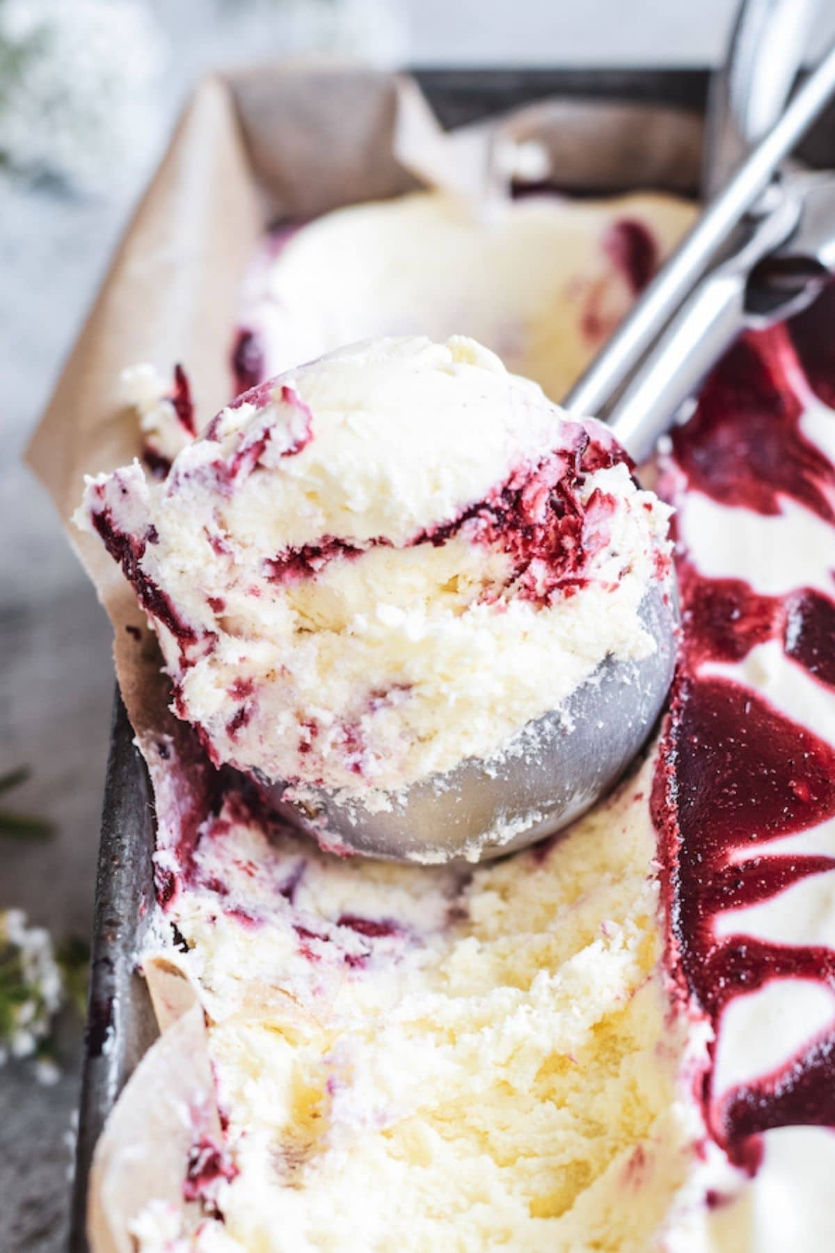 a close up of a silver scoop with blackberry ice cream.