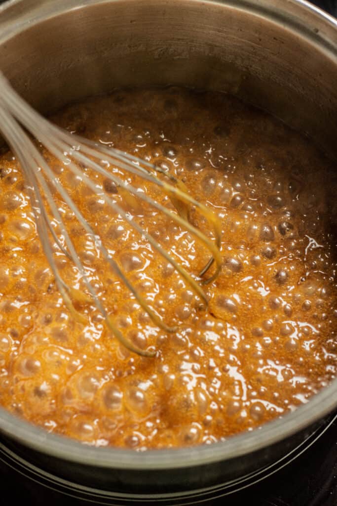 bubbling caramel sauce in a pot with a whisk.