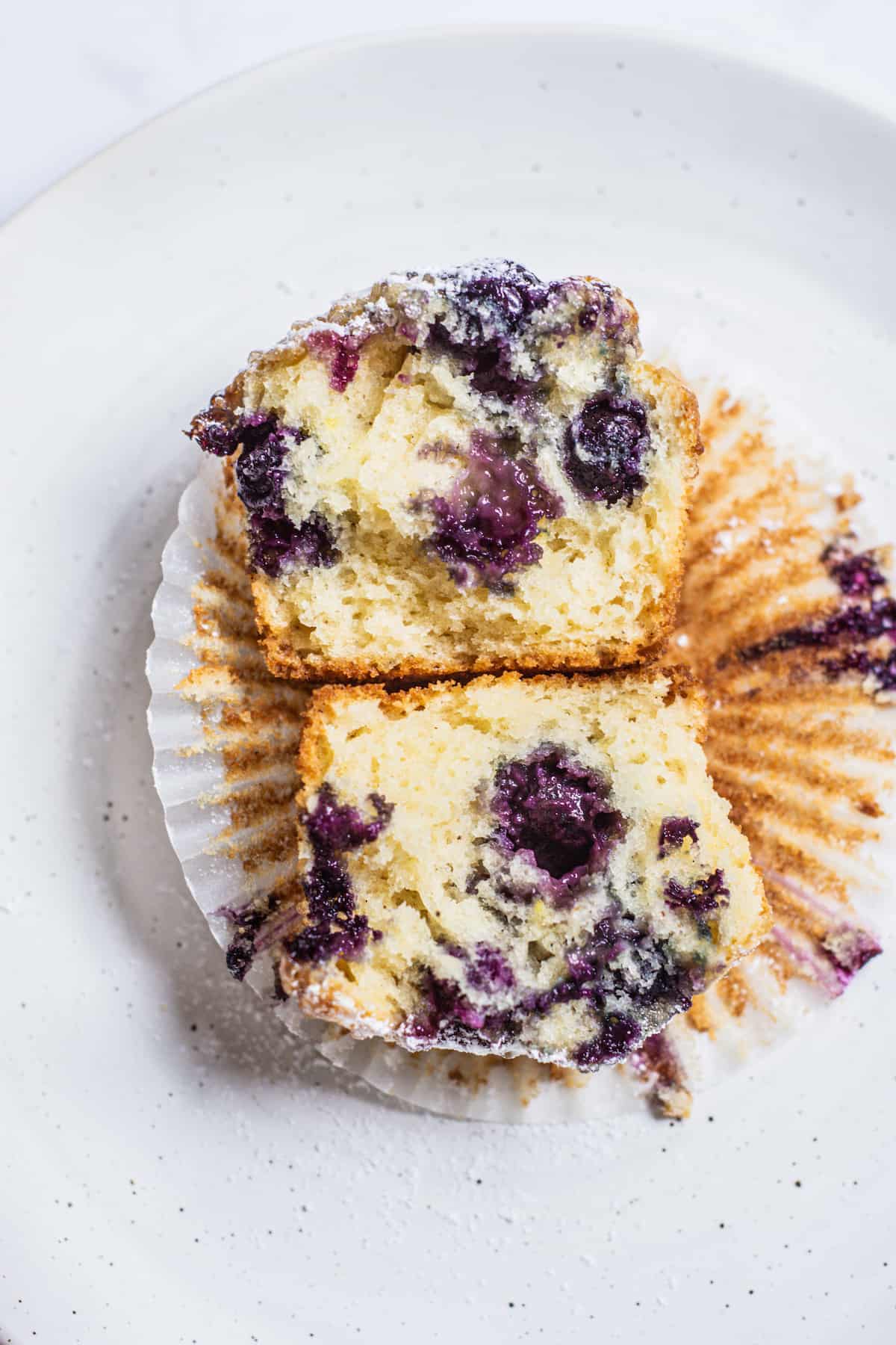 open blueberry muffin with purple berries against yellow muffin.
