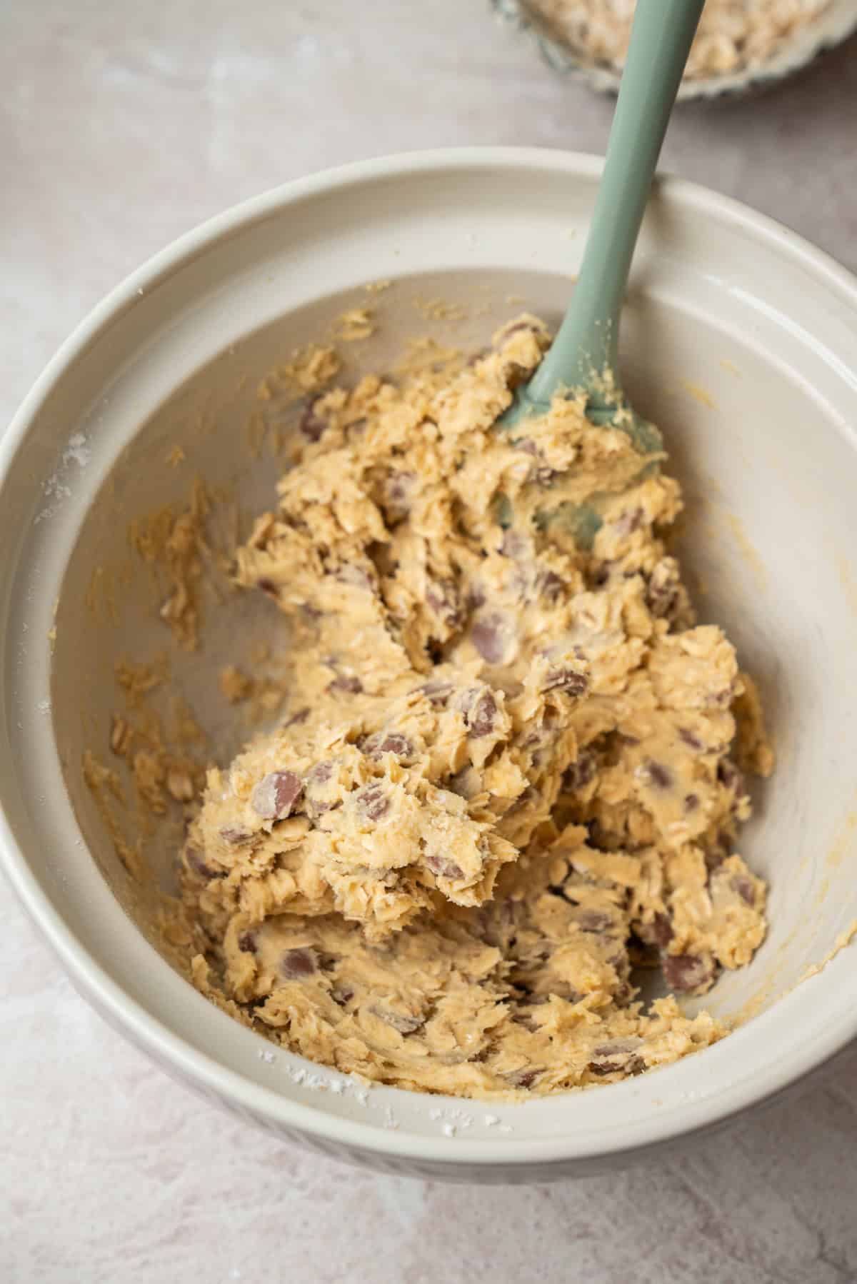 A silicone spatula resting in a mixing bowl filled with raw oatmeal chocolate chip cookie dough.