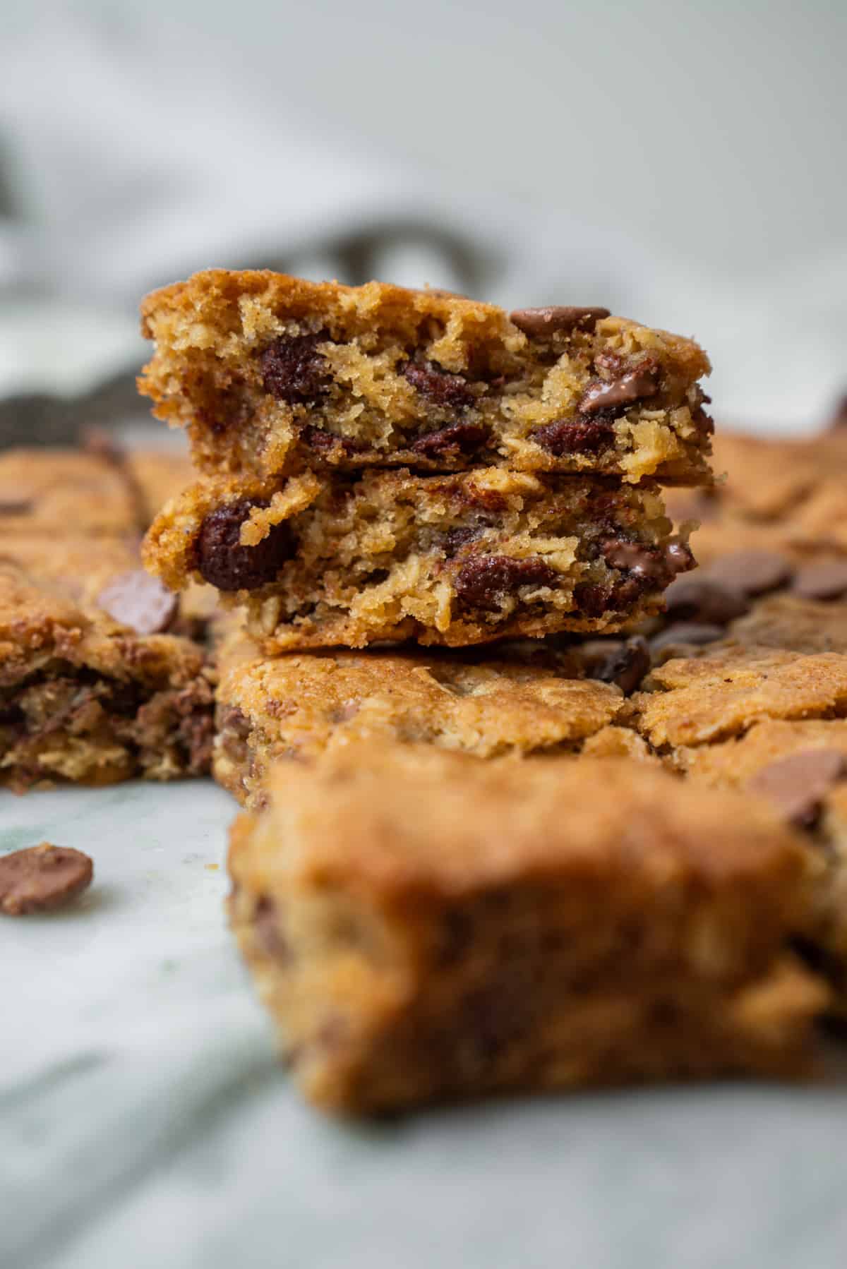 A stack of two oatmeal chocolate chip bars with visible chocolate chips, sitting among other cut bars.
