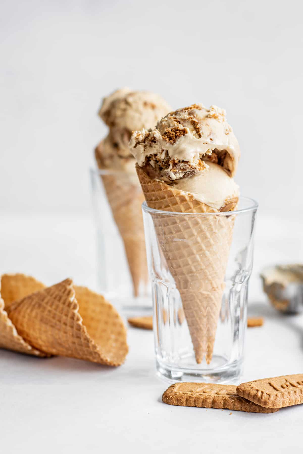 side views of ice cream cones in a glass with cookies in the foreground.