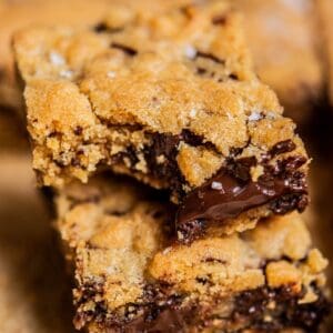 Close-up of two gooey brown butter chocolate chip bars stacked on top of each other, with melted chocolate visible inside the soft, golden-brown cookie layers.