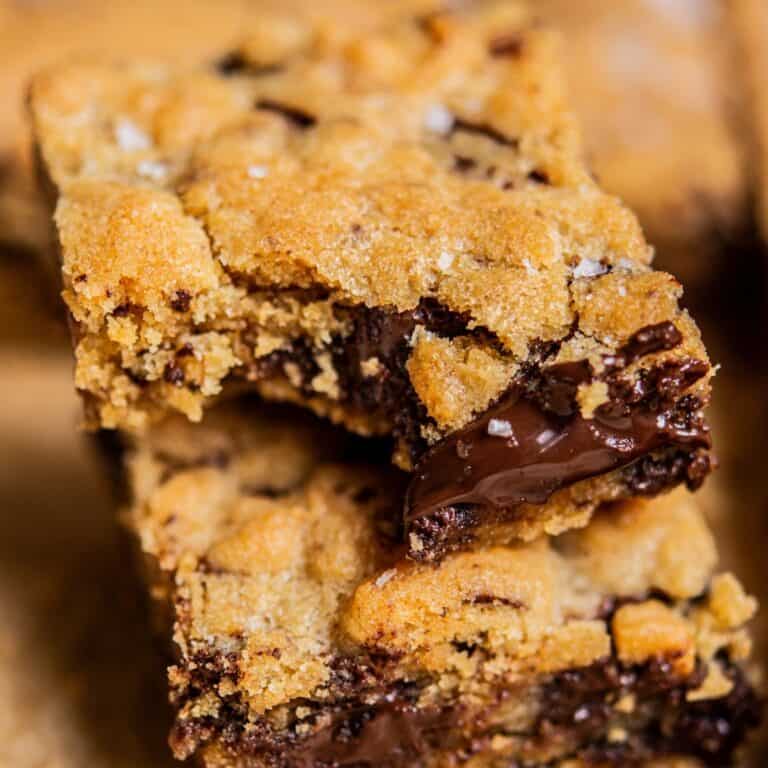 Close-up of two gooey brown butter chocolate chip bars stacked on top of each other, with melted chocolate visible inside the soft, golden-brown cookie layers.