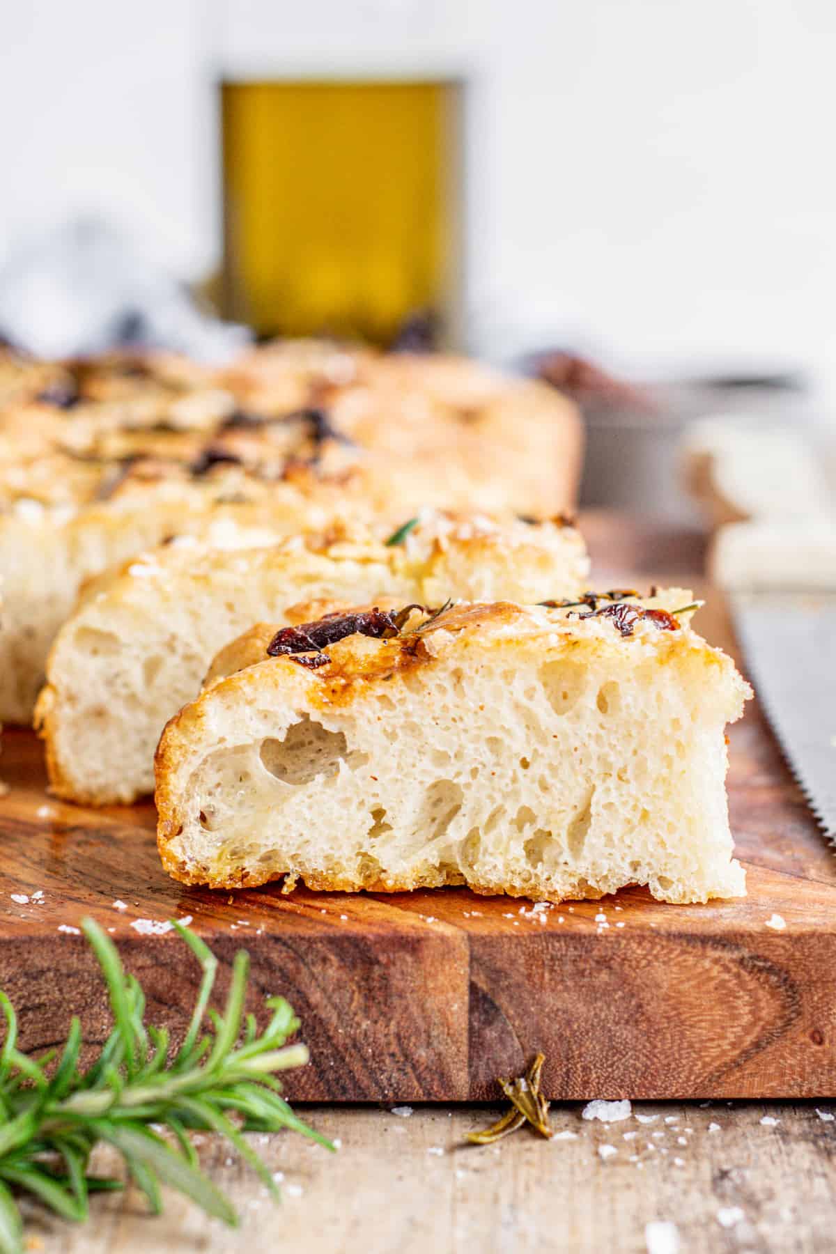 sliced focaccia bread with rosemary in the forefront.