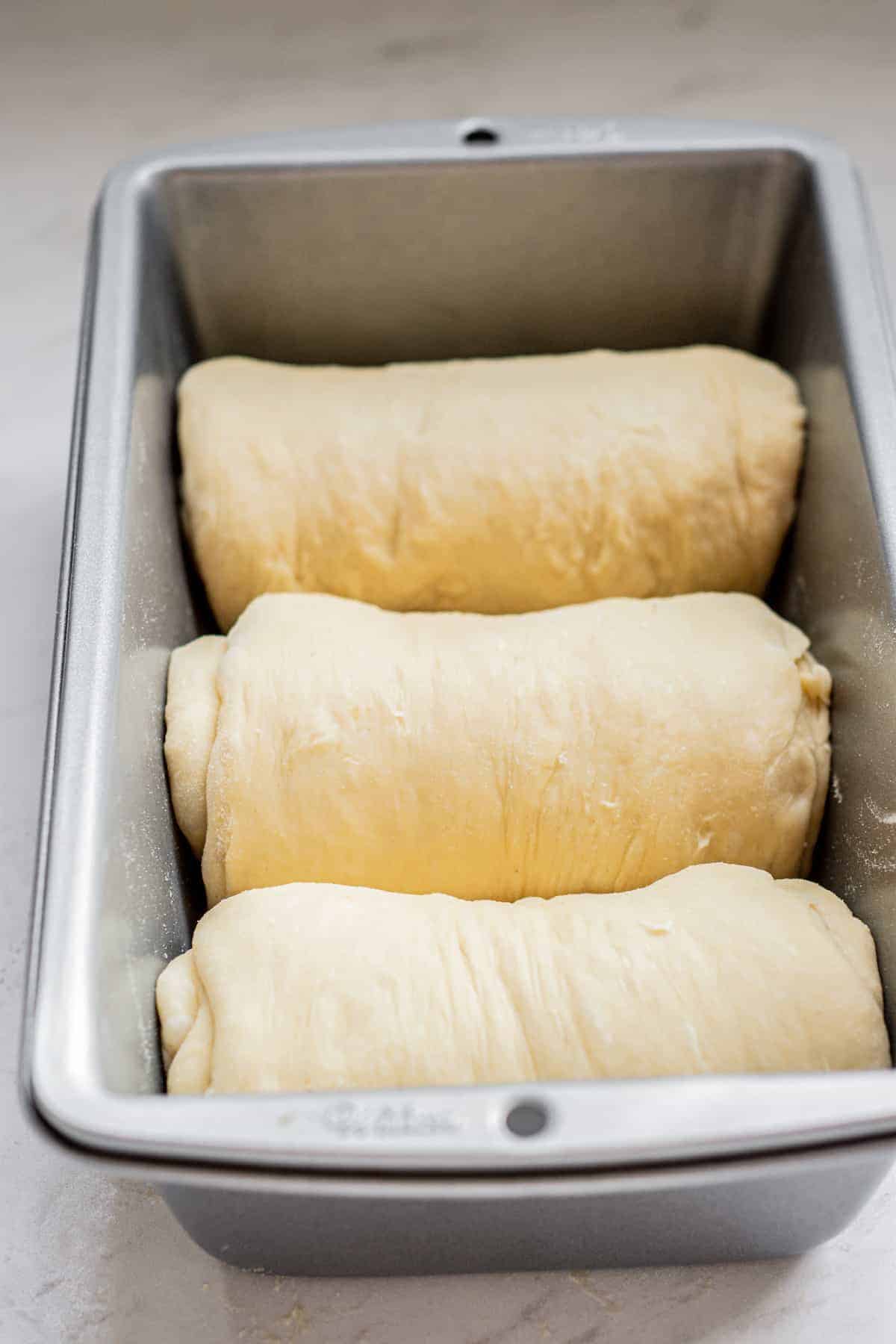 milk bread rolls in a pan waiting to rise.